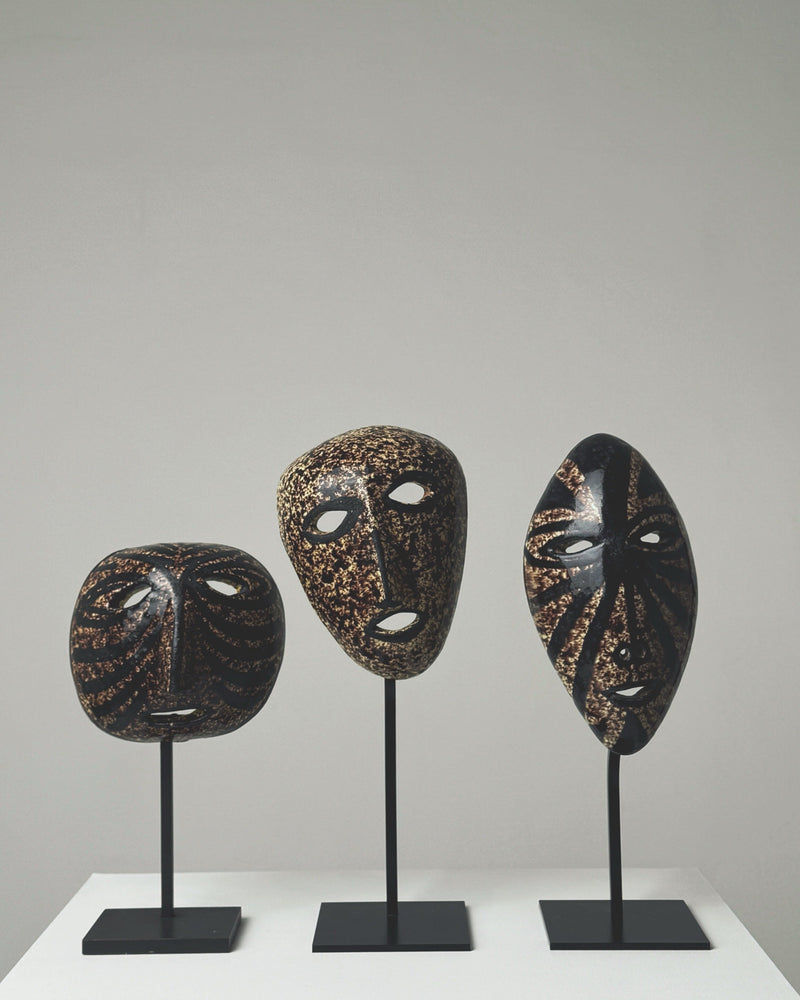 Three black ceramic masks with gold speckled patterns on stands