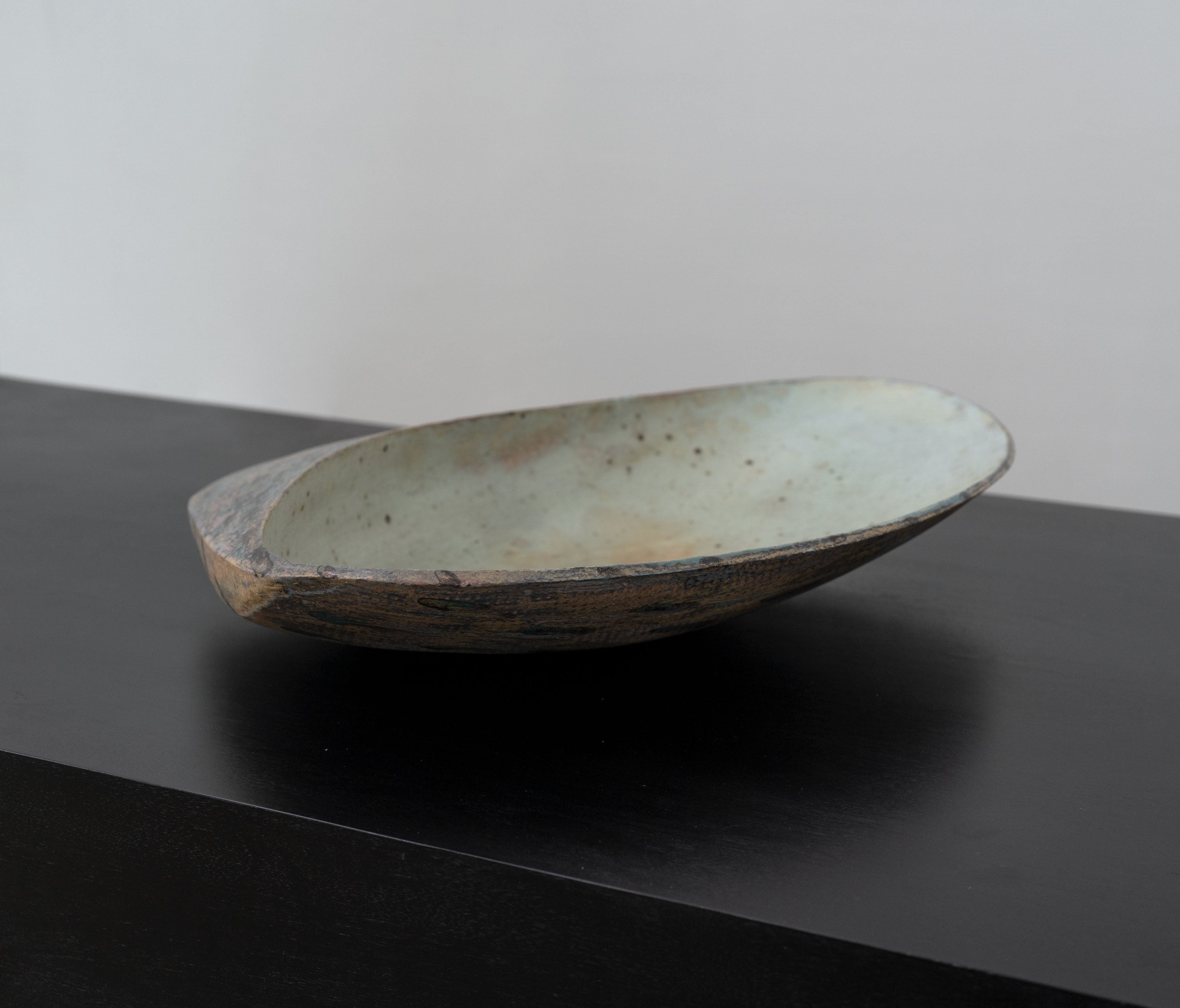 Large ceramic bowl with weathered finish on black surface, profile view