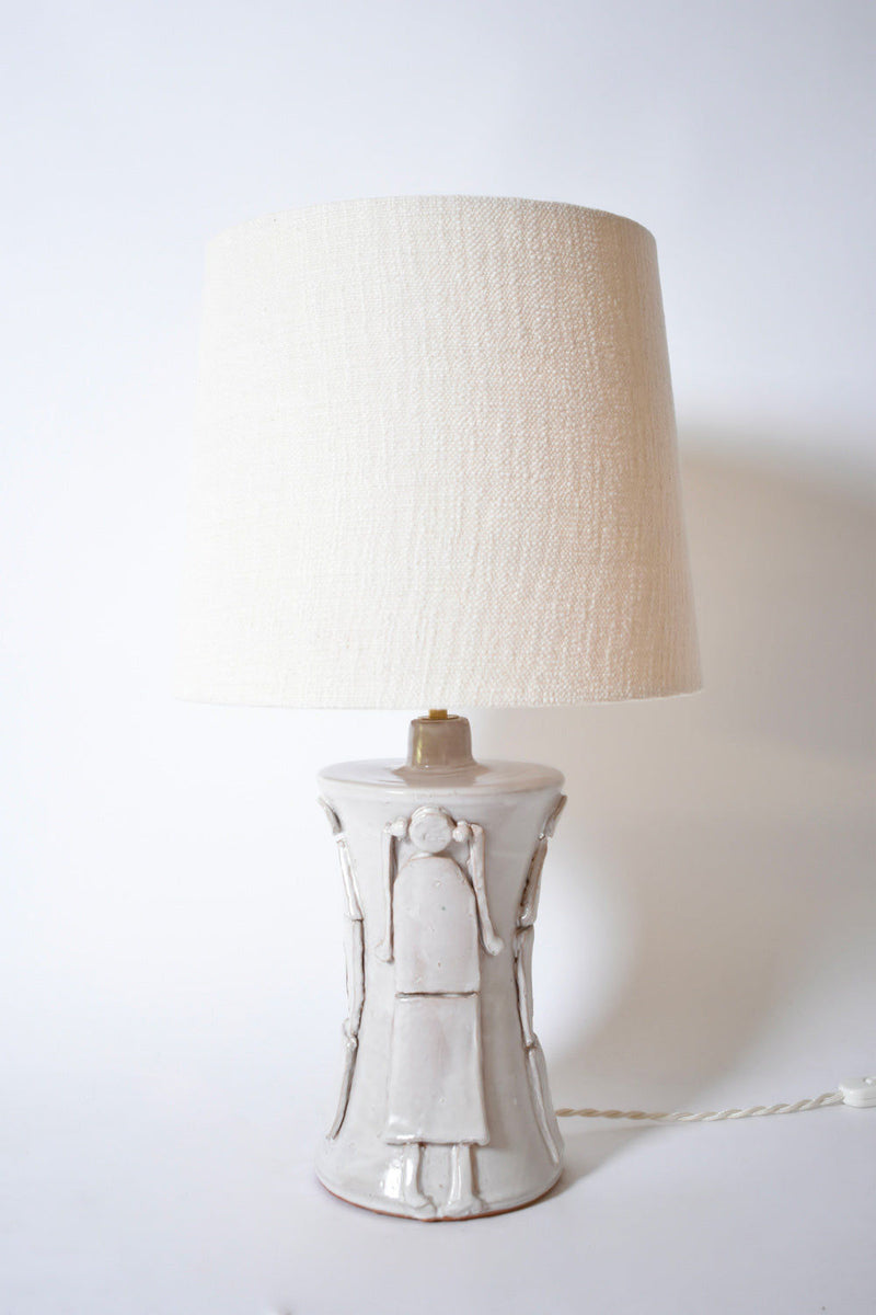 The "Kasaï" Avignon Ceramic Table Lamp by Barracuda Interiors features an off white sculpted ceramic base with simple, raised human figure designs and a textured shade—an elegant, customizable accent for any interior.