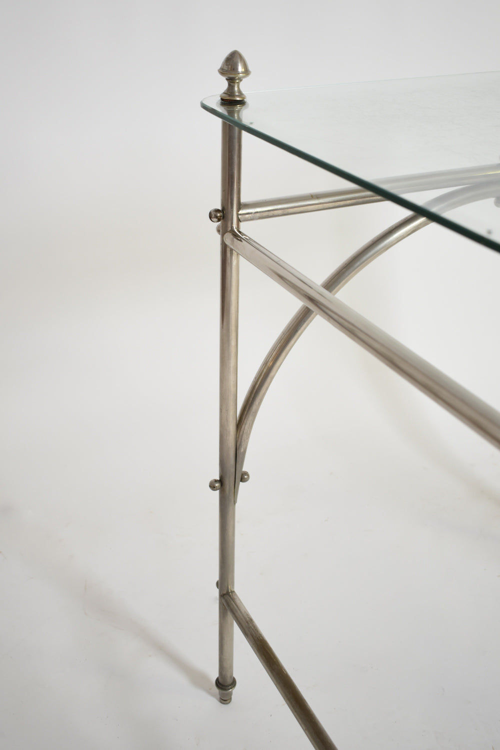 A close-up of the Tubular Chrome Iron and Glass Table by Barracuda Interiors, 1920s, shows its chrome corner with decorative finial, silver metal legs, and glass top set against a white background in classic vintage style.
