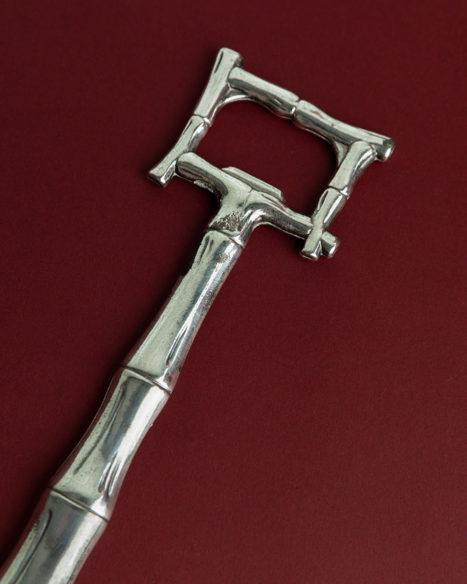 Vintage 1970s Silver Plated Bottle Opener, Bamboo Design — close-up on maroon background
