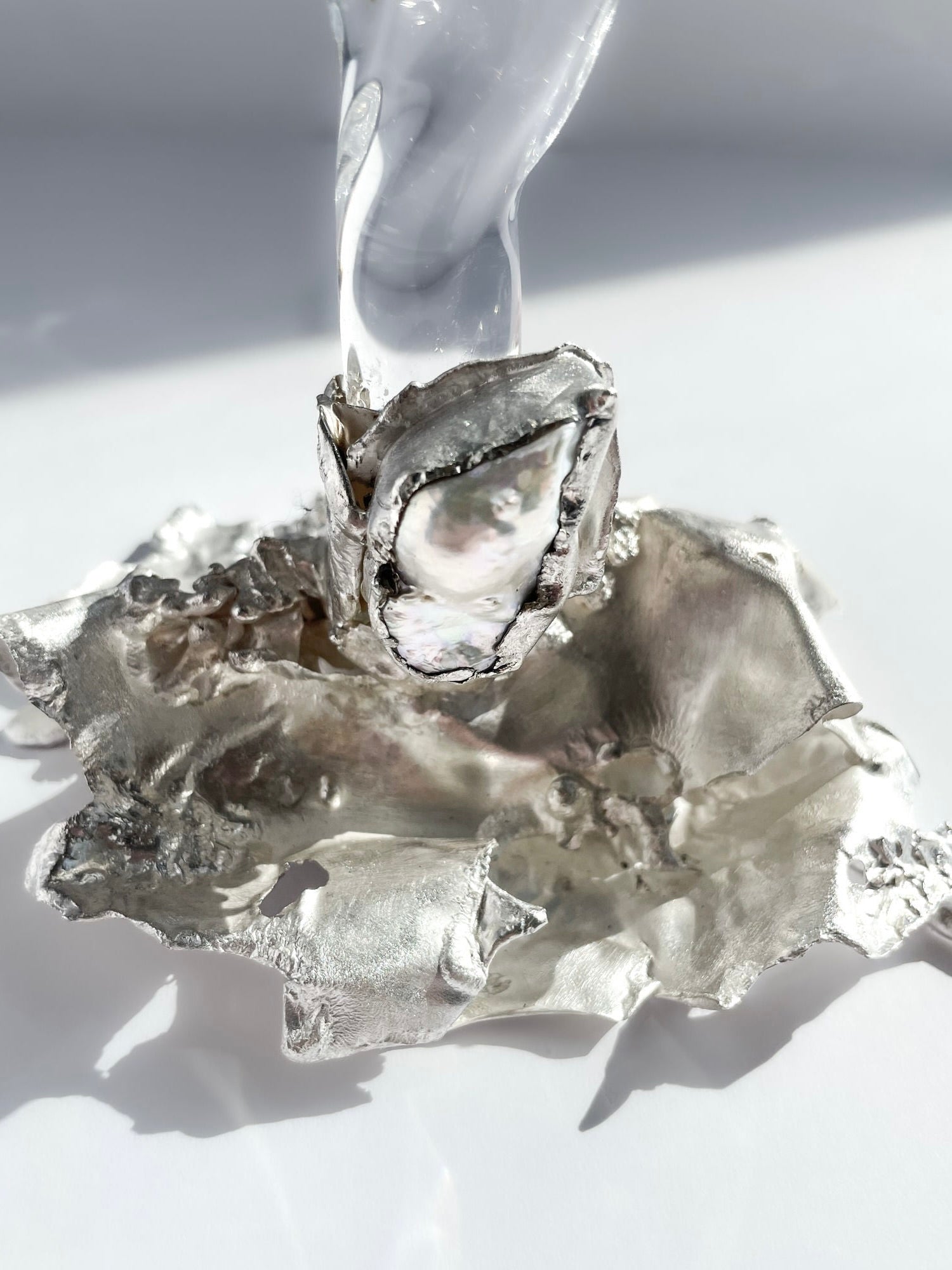 Jewelled Goblet no. 10 by Szkło Studio x Lindsey Fontijn features a shiny, irregular metallic base with a smooth hand-blown glass element, shown in close-up against a bright white background.