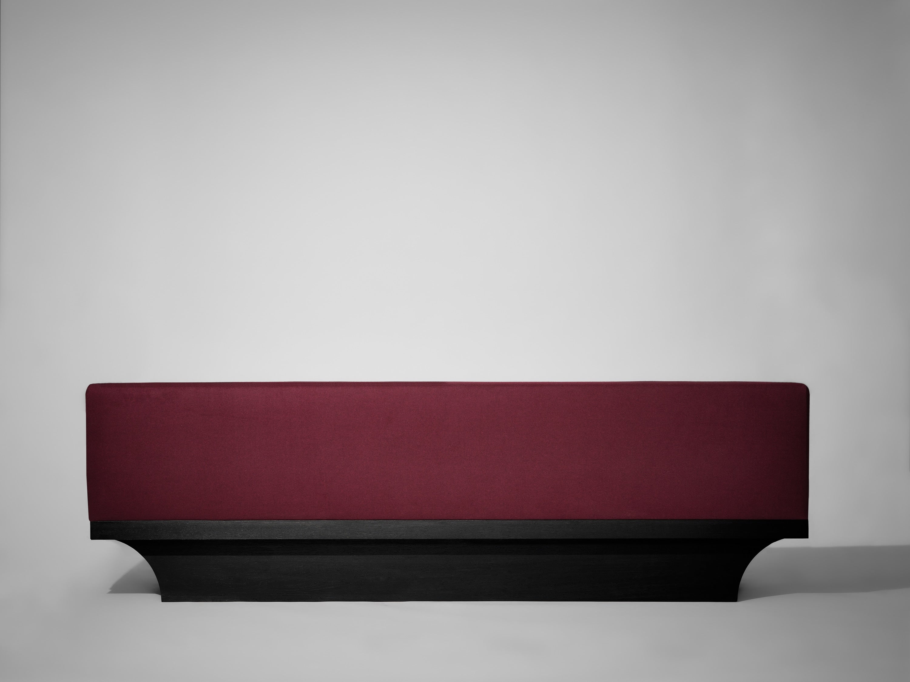The Mokko Acer Sofa, a minimalist maroon bench with a solid black base, is set against a plain light gray background.