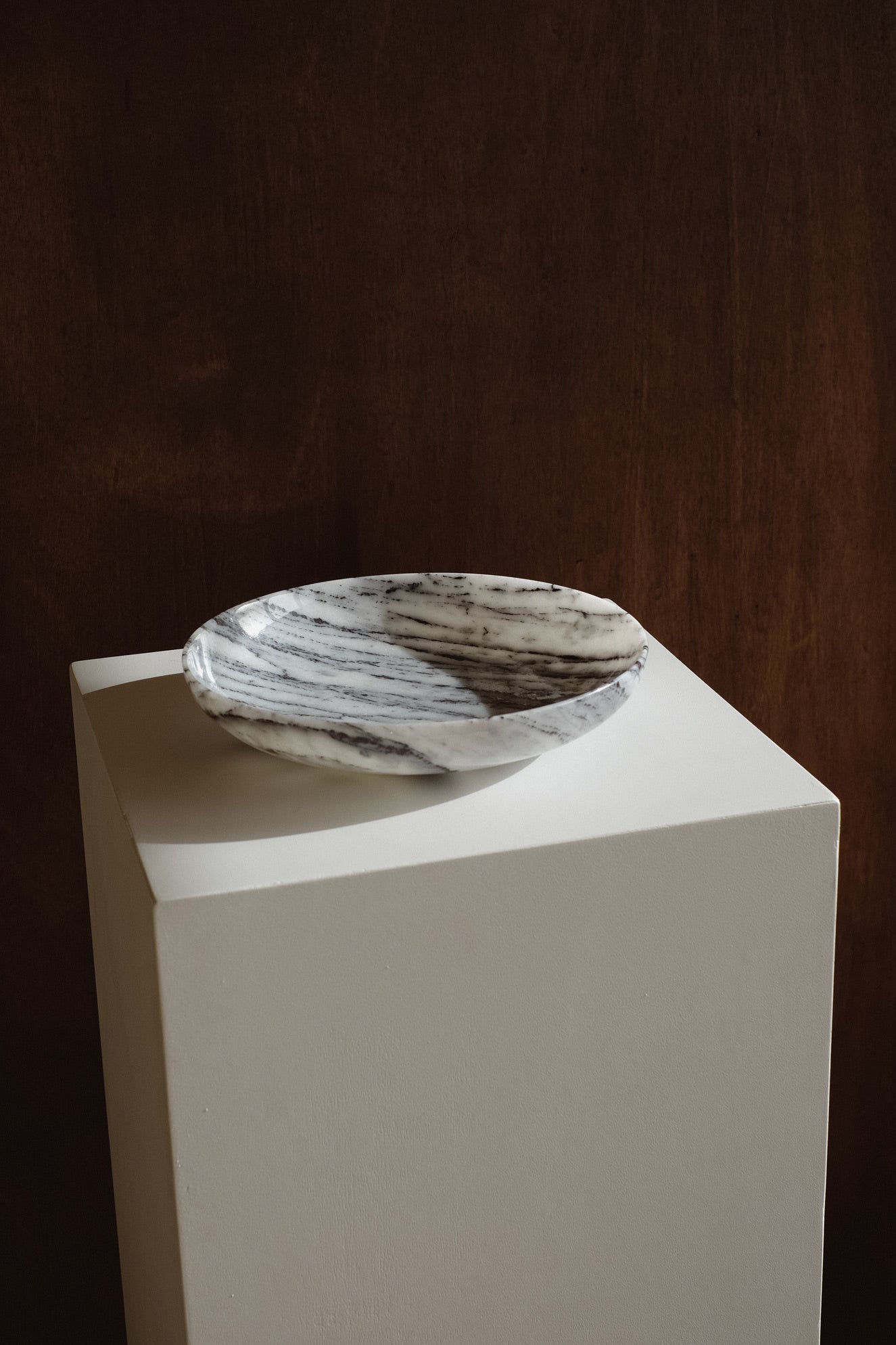 Marble Bowl — side angle on white pedestal against dark background