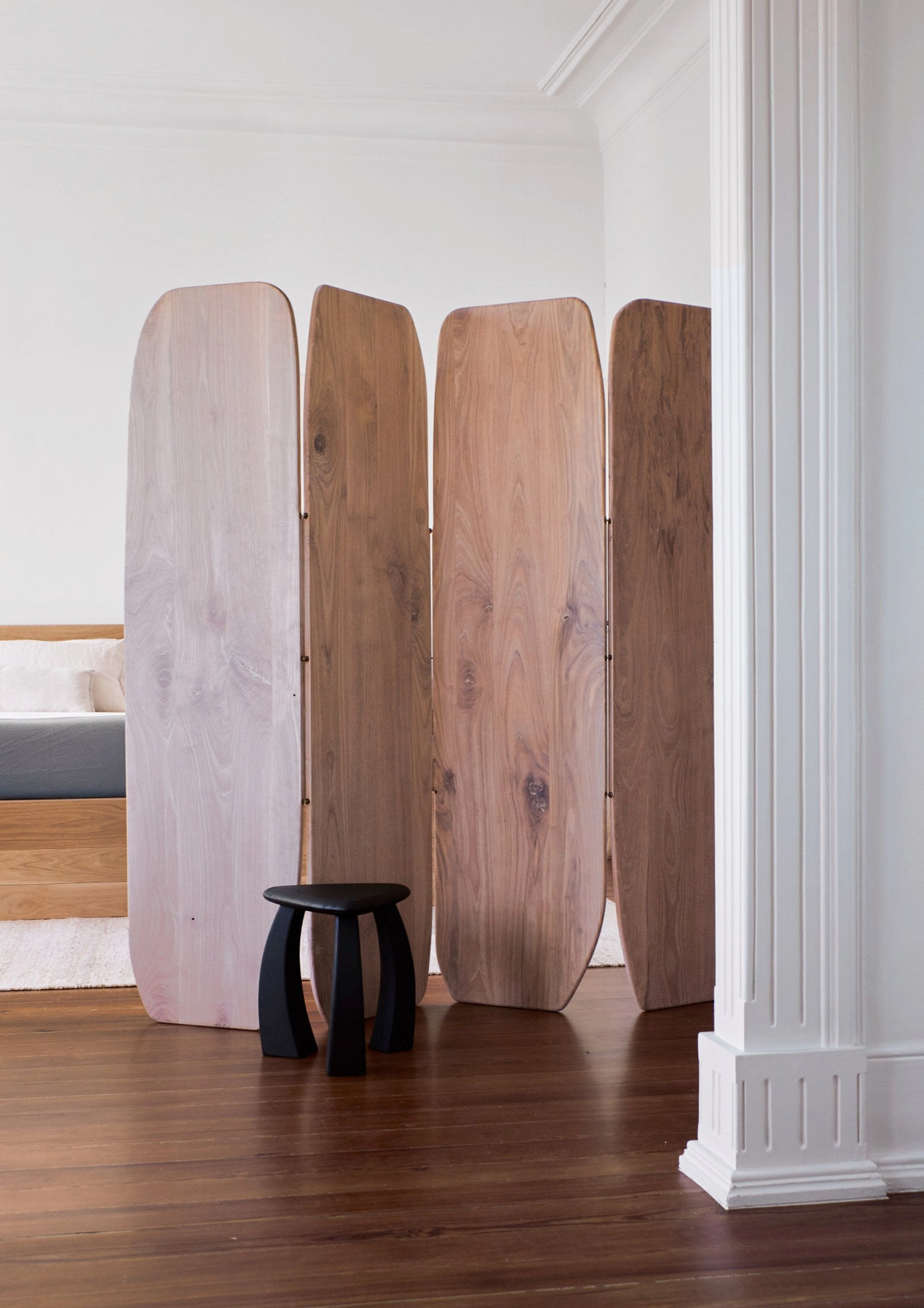 Arc de Stool '37 — black stool beside wooden room divider