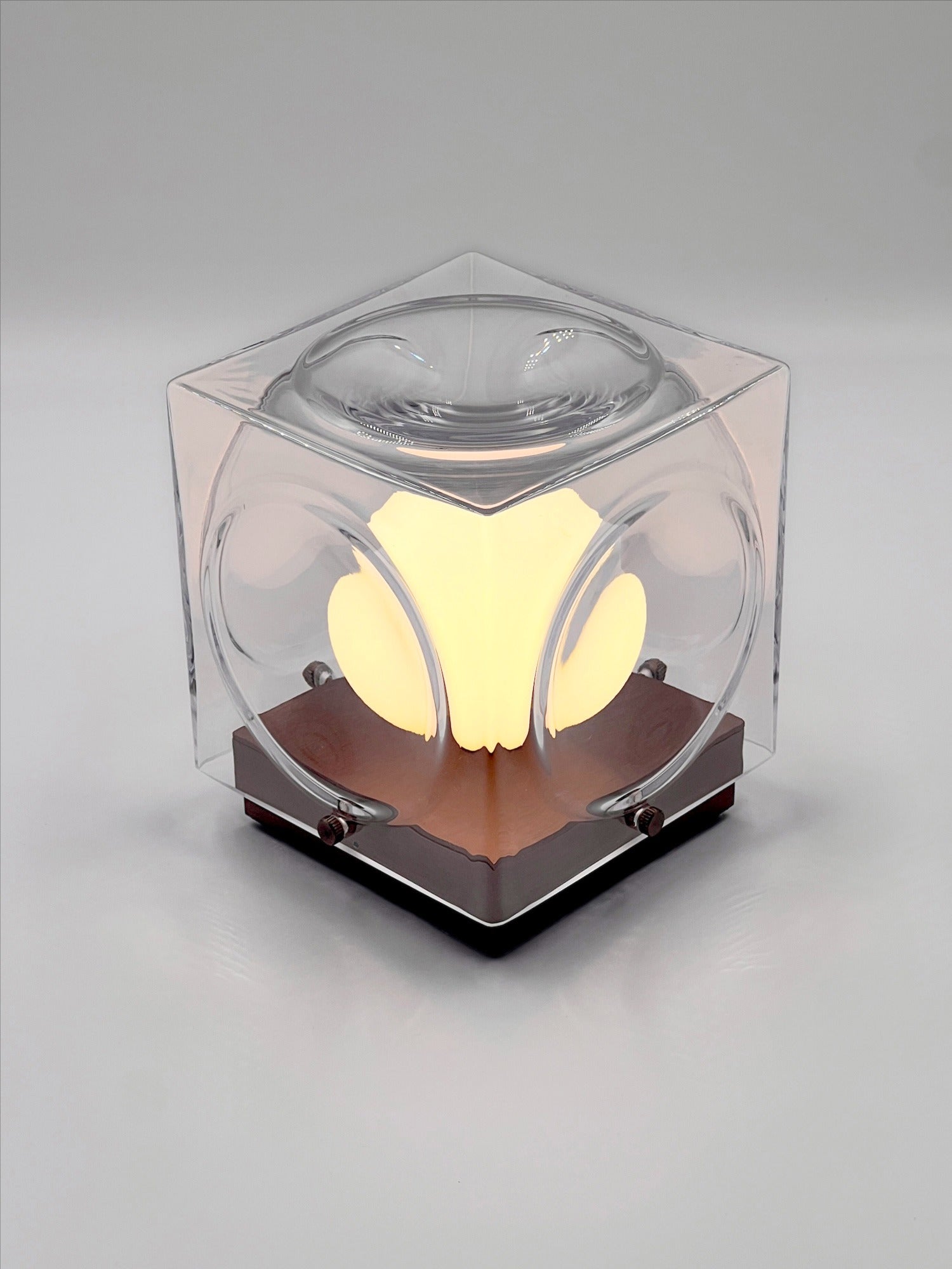 The Chant Portable Table Lamp by Lee Broom features a modern cube design with a clear outer shell, glowing center, and dark square base, shown against a plain gray background.