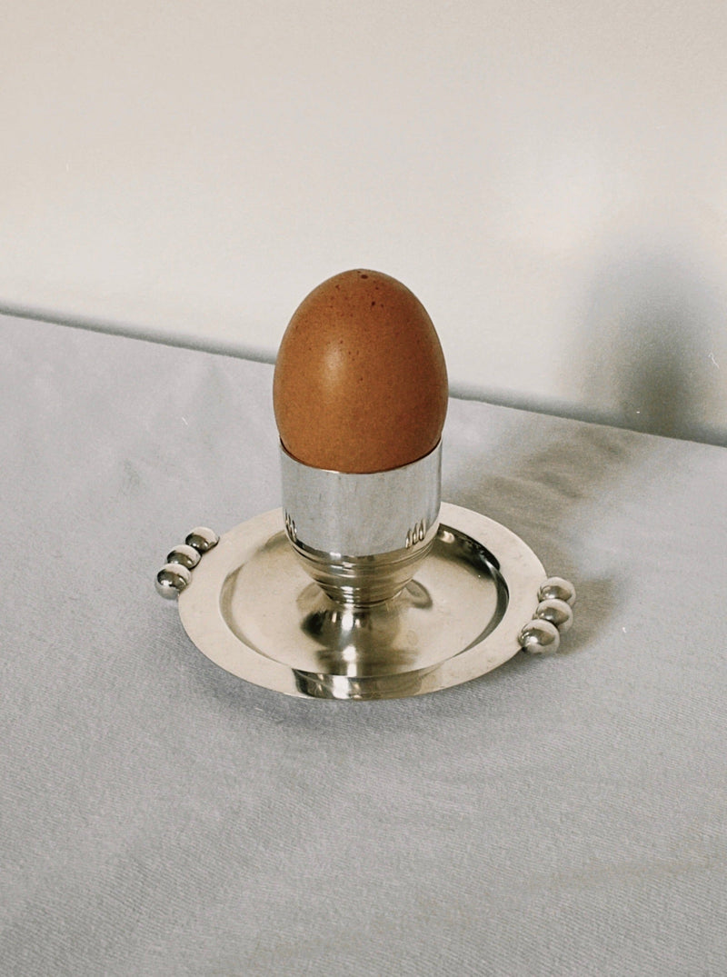 Silver plated egg cup with decorative handles holding brown egg