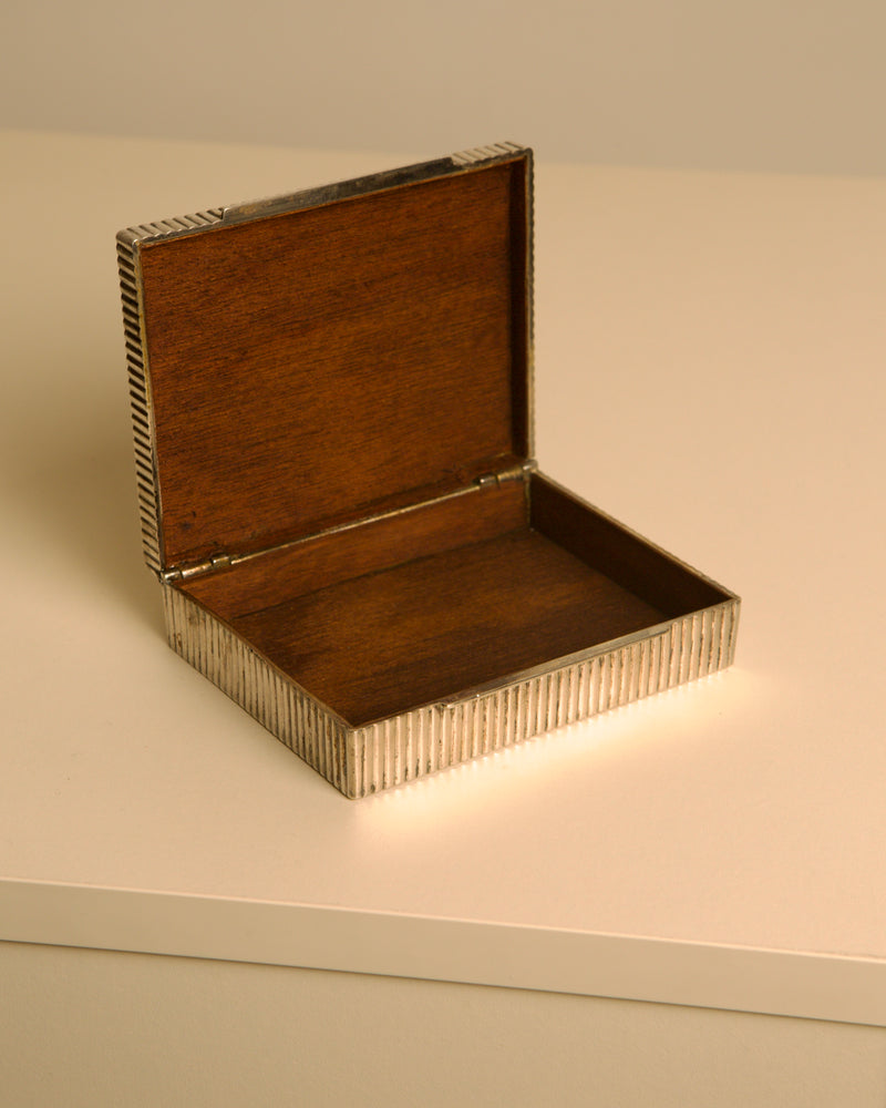 Open fluted metal box revealing warm wooden interior detail
