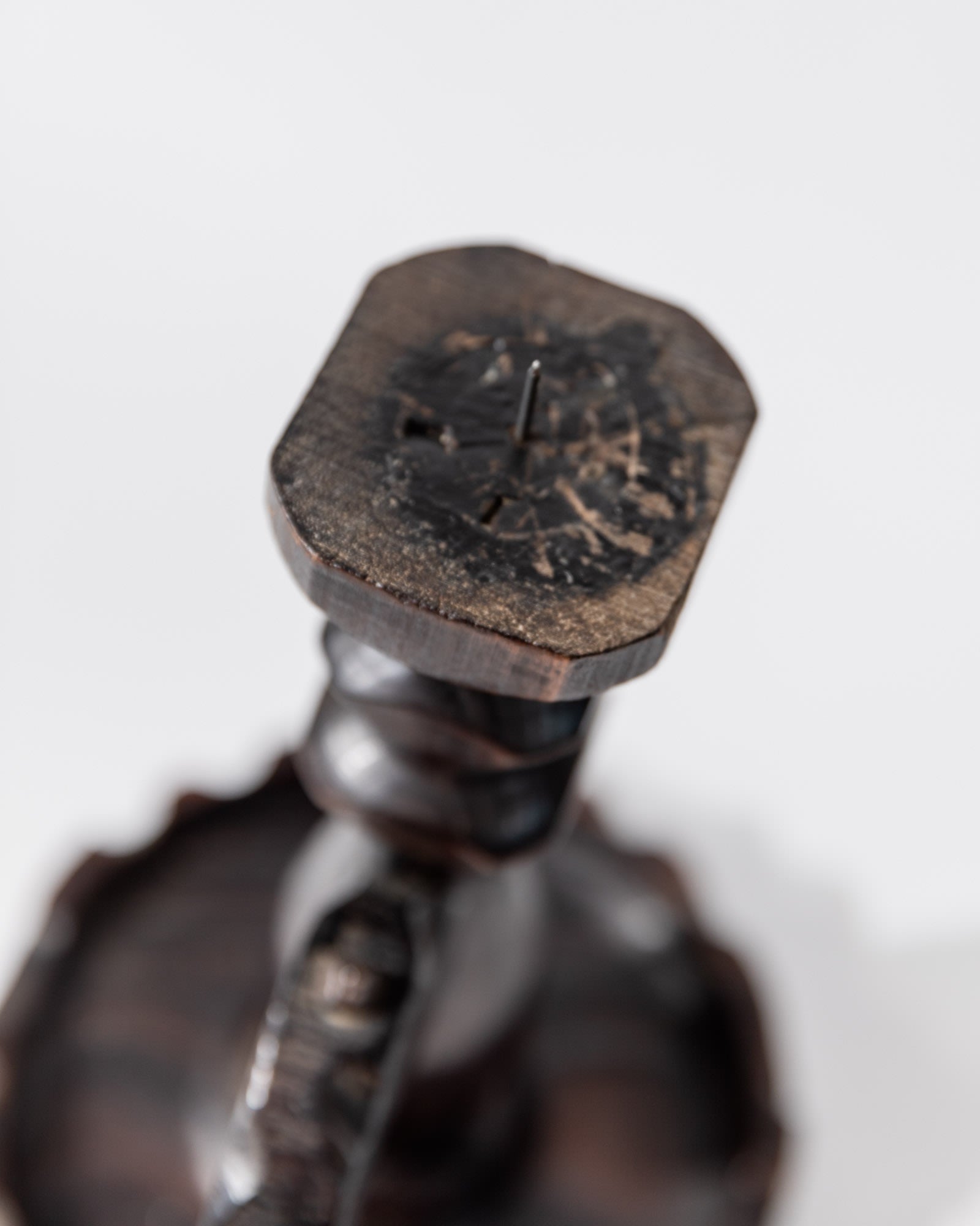 Close-up of the base of a 1960s Bottega Jacobs Wooden Candleholder in handcarved dark wood, showing the textured grain, central nail, and vintage wear; background is plain and out of focus.