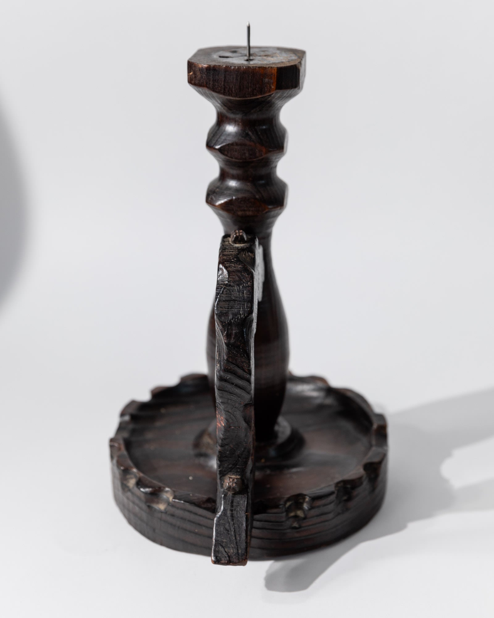 The 1960s Wooden Candleholder in Handcarved Dark Wood by Bottega Jacobs features a pointed central spindle, scalloped round base, and vertical wood divider, all echoing Brutalist design. It casts a distinct shadow against a light background.