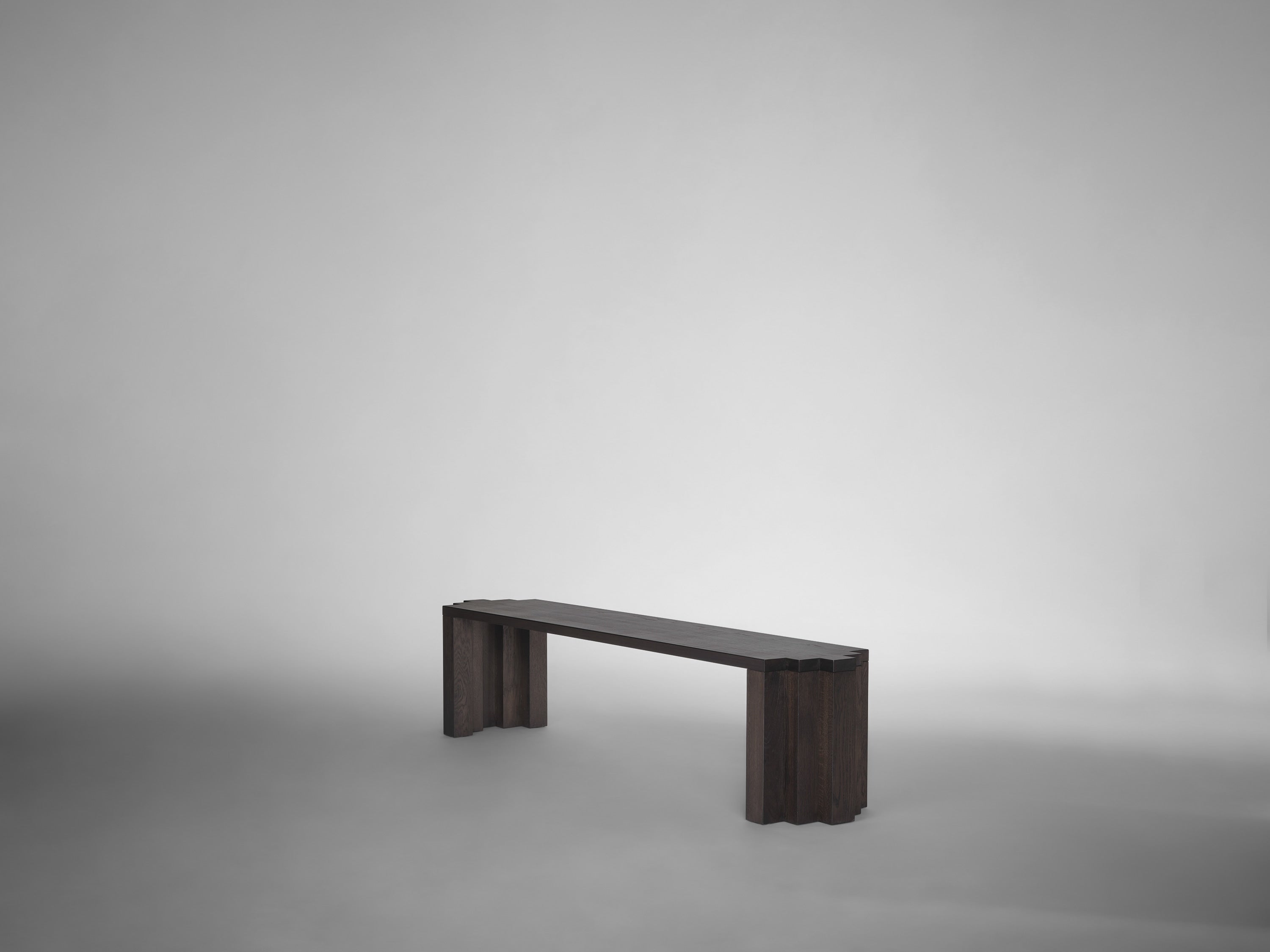 The Cadence Bench by Mokko, made from solid European oak, features minimalist scalloped edges and clean lines. Set against a light gray backdrop, this customizable piece offers a striking yet understated presence.