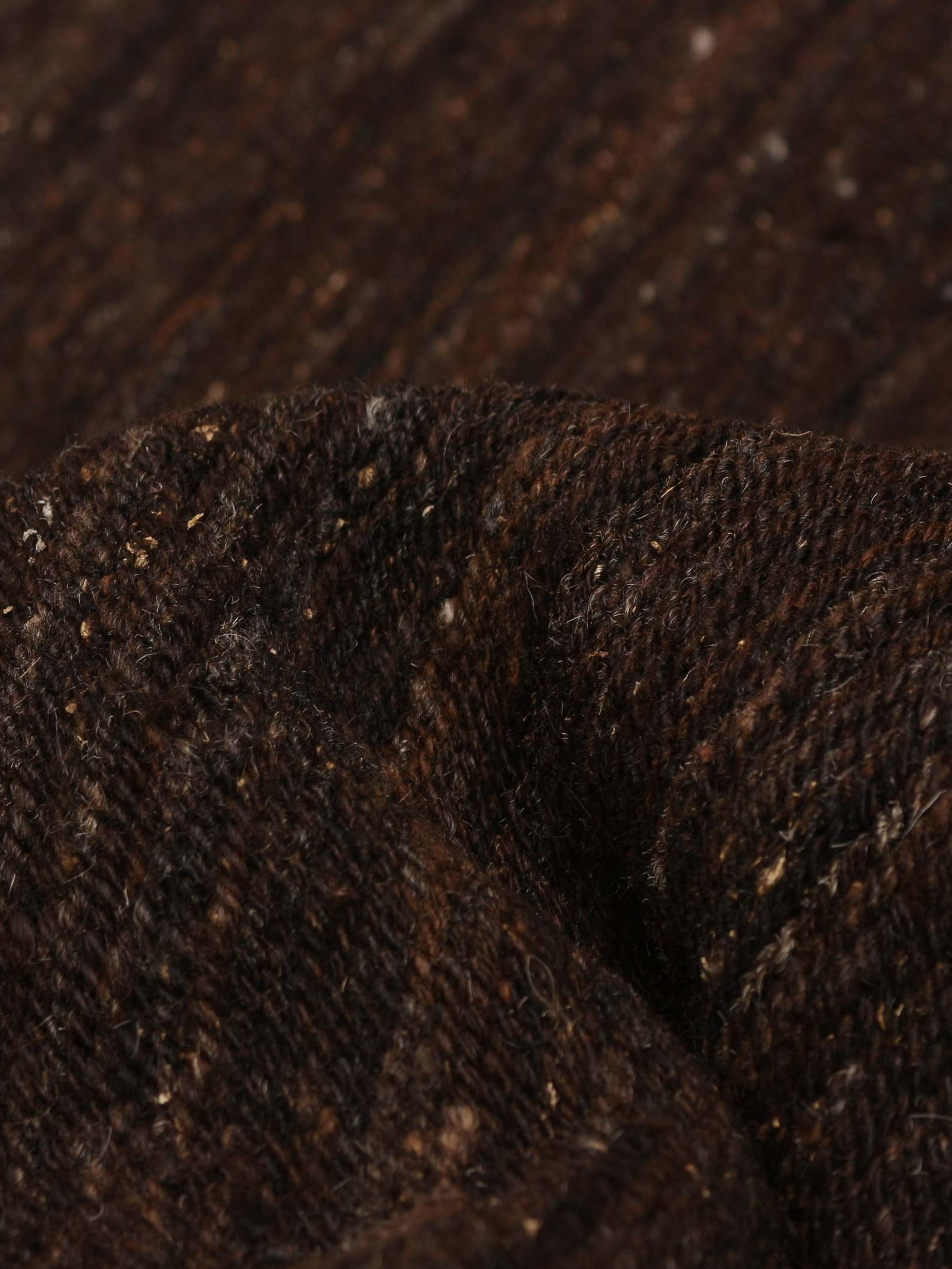 Close-up of a Flatweave Rug in Walnut by catalog:three, 244 x 292 cm. This dark brown textured fabric with subtle stripes mirrors a hand-woven kilim. Its raised, soft surface folds into gentle curves and shadows, highlighting its unique craftsmanship.