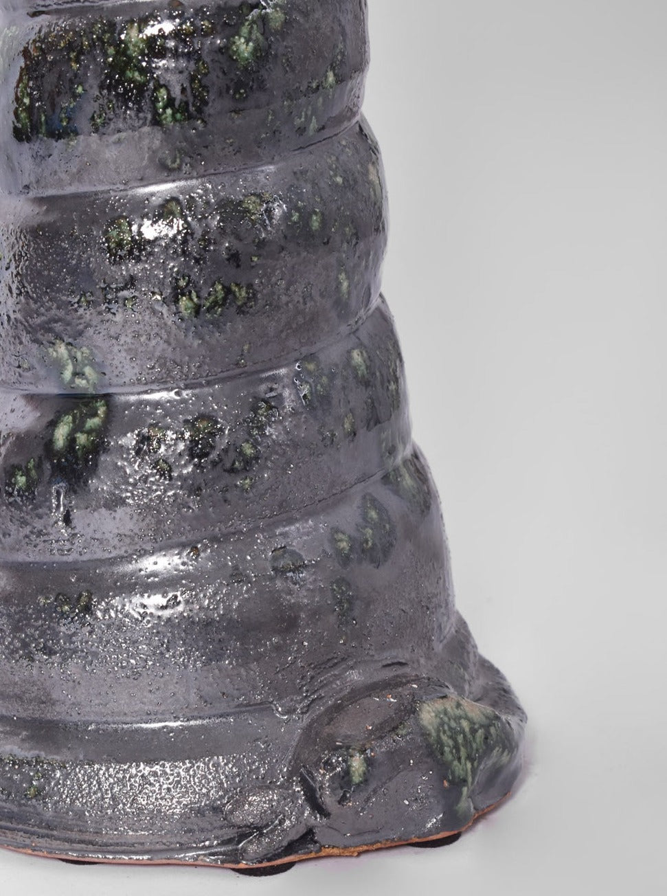 Close-up of the "Teotihuacan" Green Ceramic Table Lamp from Barracuda Interiors' Barracuda Edition, featuring a shiny dark gray ridged body with green speckles, inspired by Teotihuacan artifacts, set against a plain light gray background.