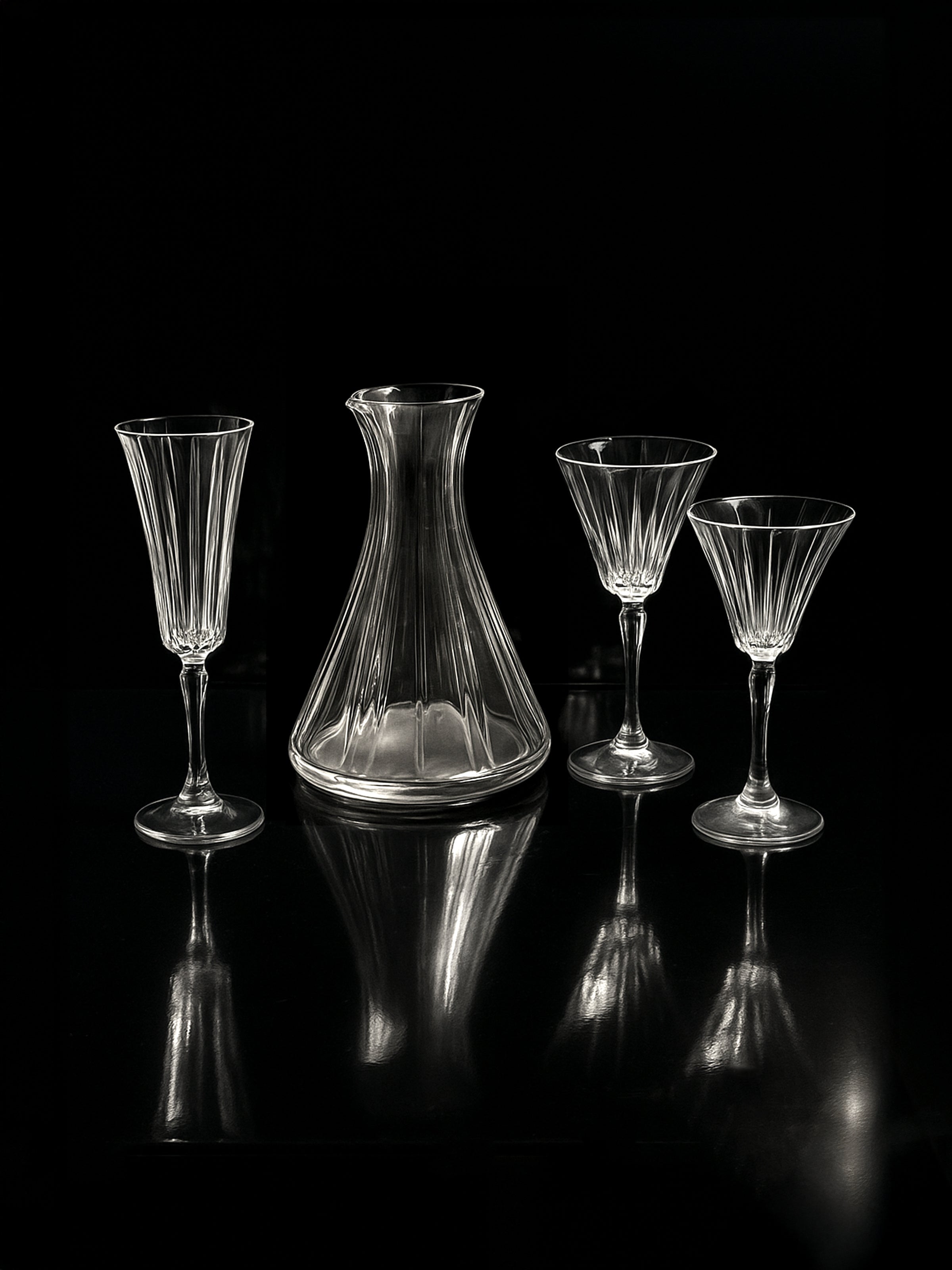 The Dodo Vintage Italian champagne and wine crystal set with hand-cut glasses and carafe is displayed on a reflective black surface against a dark background.