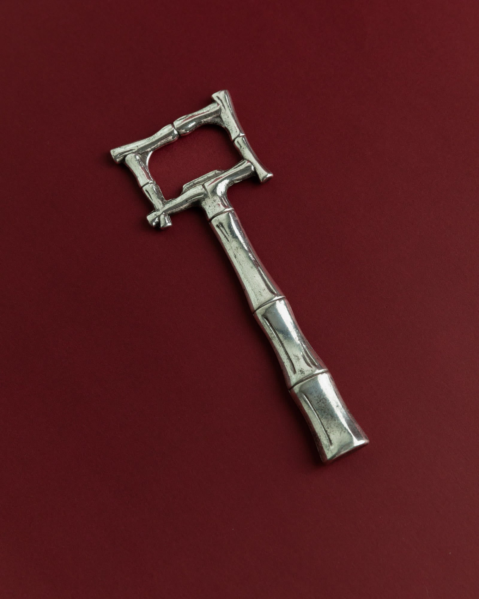 Vintage 1970s Silver Plated Bottle Opener, Bamboo Design — side angle on burgundy background