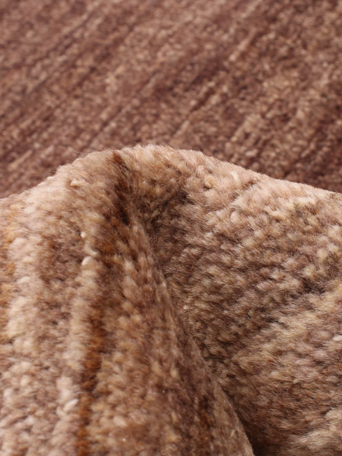 Close-up of the catalog:three Ziegler Rug in Willow (247 cm x 327 cm) reveals its soft, brown, and cream-colored texture reminiscent of a plush, furry fabric. Draped and folded, it showcases rich, warm tones and a cozy texture.