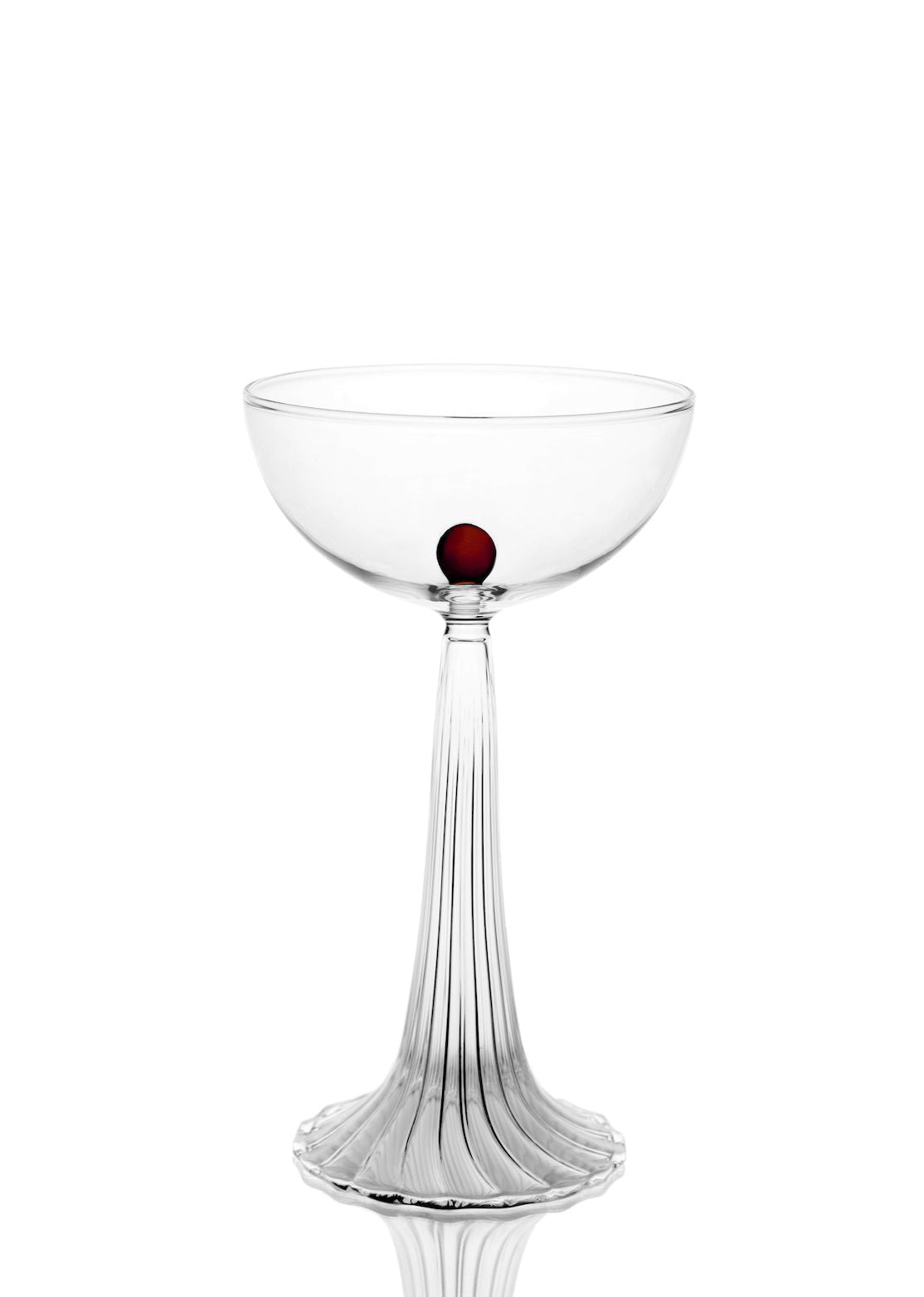 The Nereida — Coupe Glass by Agustina Bottoni features clear borosilicate glass, a fluted stem, and a single small red dot on the bowl, shown against a white background—a refined example of elegant drinkware.