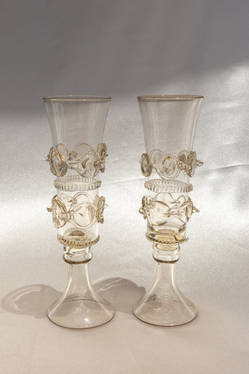 Two mouthblown Lucie Claudia Podrabska champagne flutes—Dots Spirals design—stand side by side on a light textured surface, set against a soft, neutral background.