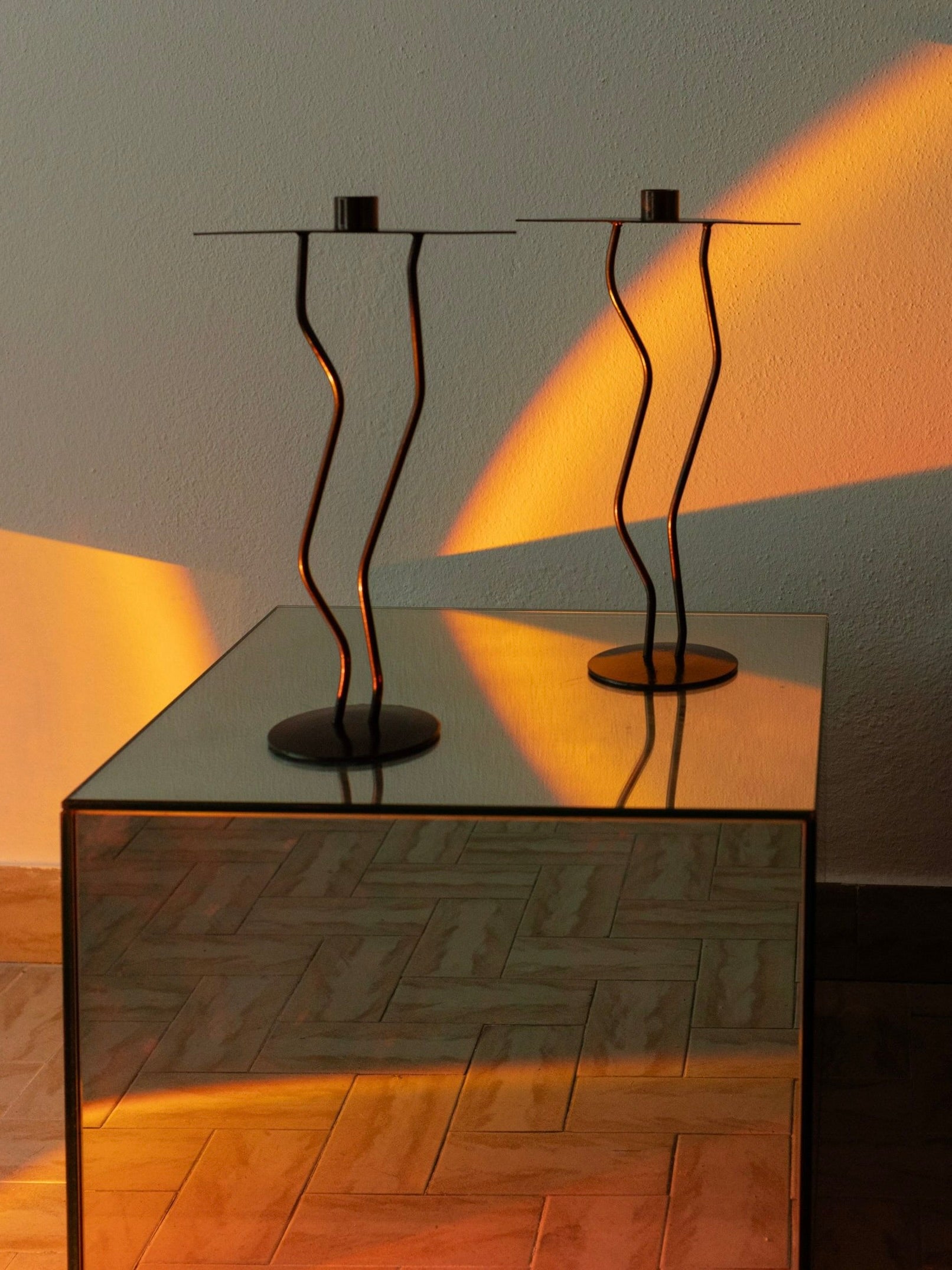 Two Metal Candlesticks Memphis Style — close-up of twisted metal design on reflective table