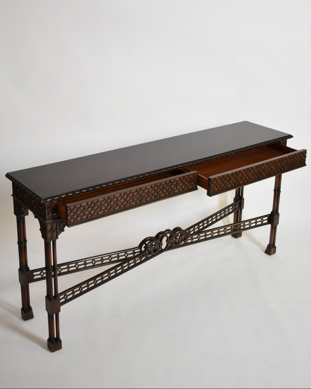 The Barracuda Interiors Carved Wood Console Table, XIXth c., features ornate patterns, two open drawers, and decorative detailing on the legs and front lattice crossbars, shown against a plain white background.
