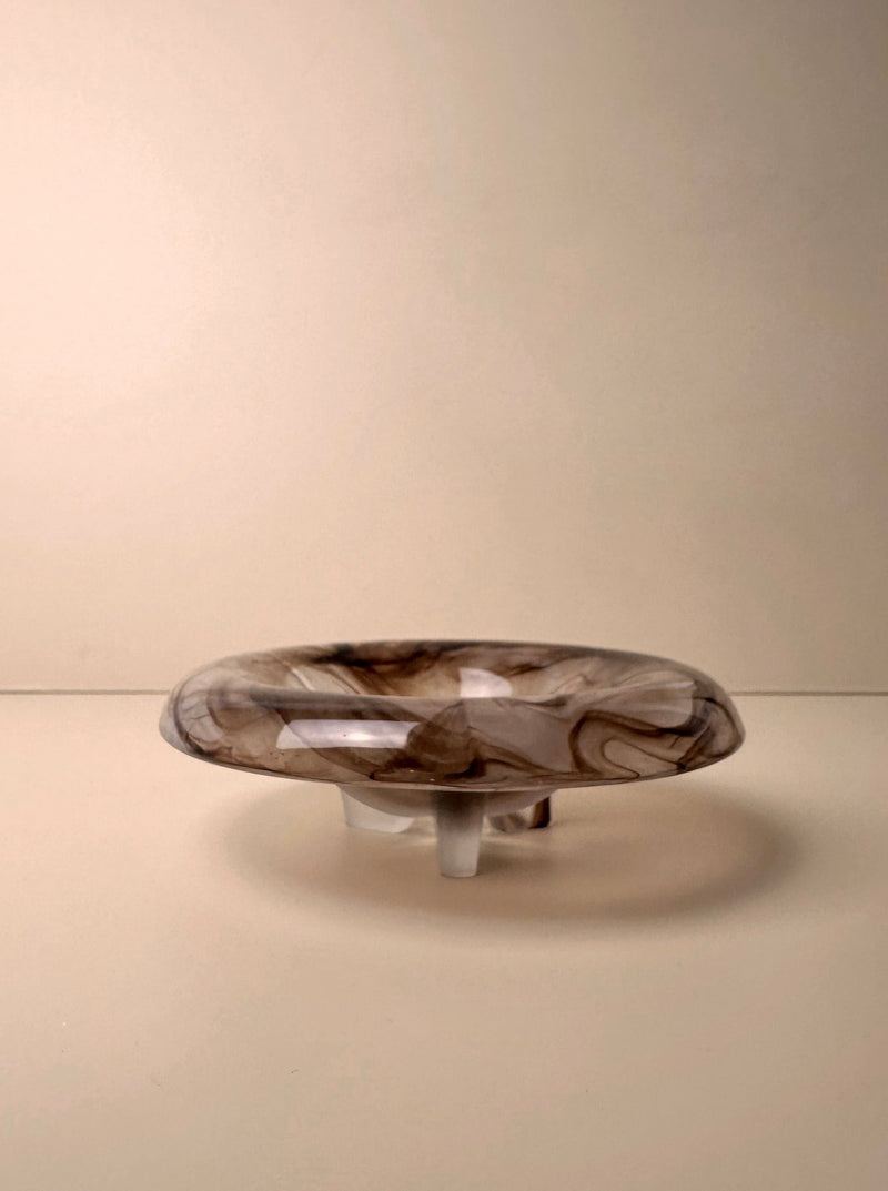 The Dodo Vintage German Art Deco Cloud Glass Bowl from around 1930 features swirling brown and cream patterns, a round shallow form, and stands on three clear legs against a plain beige background.