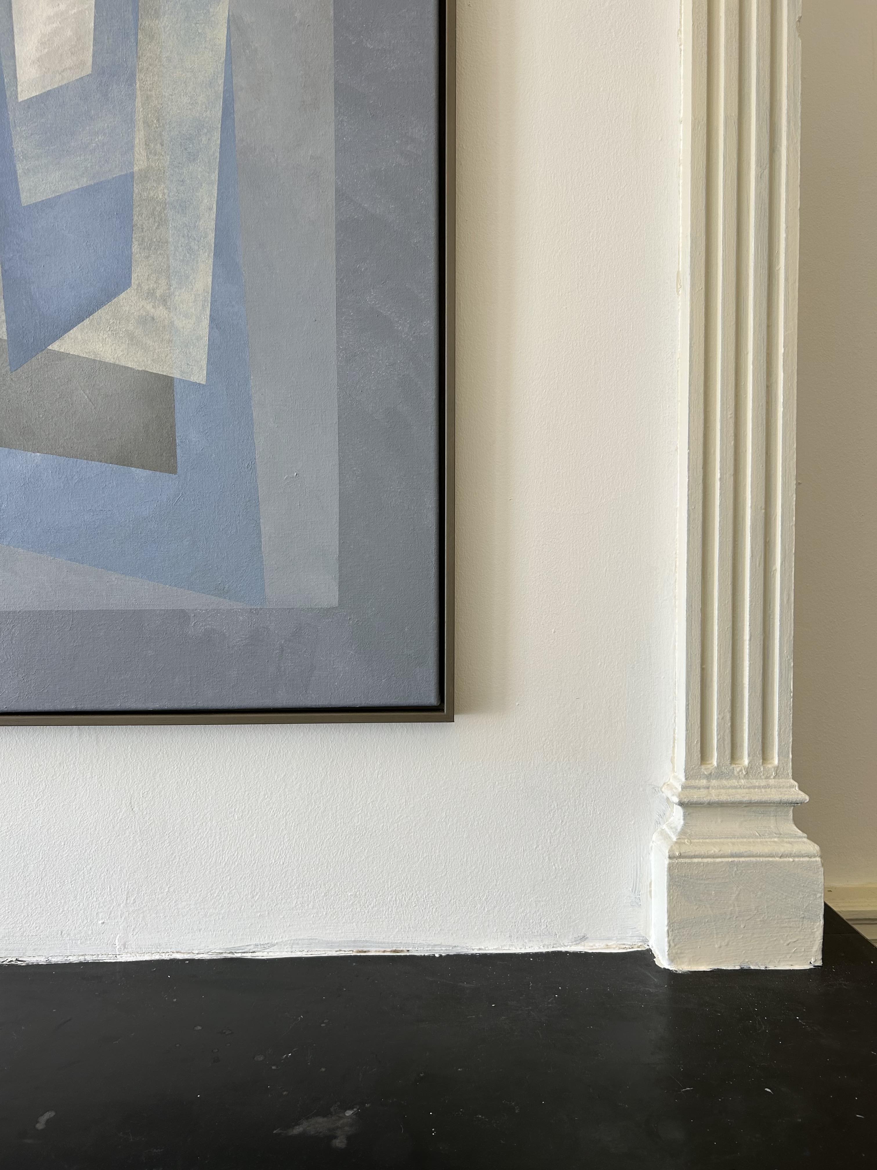 The "Floating" Painting by Iris Bavelaar, featuring overlapping blue and gray geometric shapes, is framed and displayed on a white wall near a column; its modern design is accentuated by the room’s dark, glossy floor.