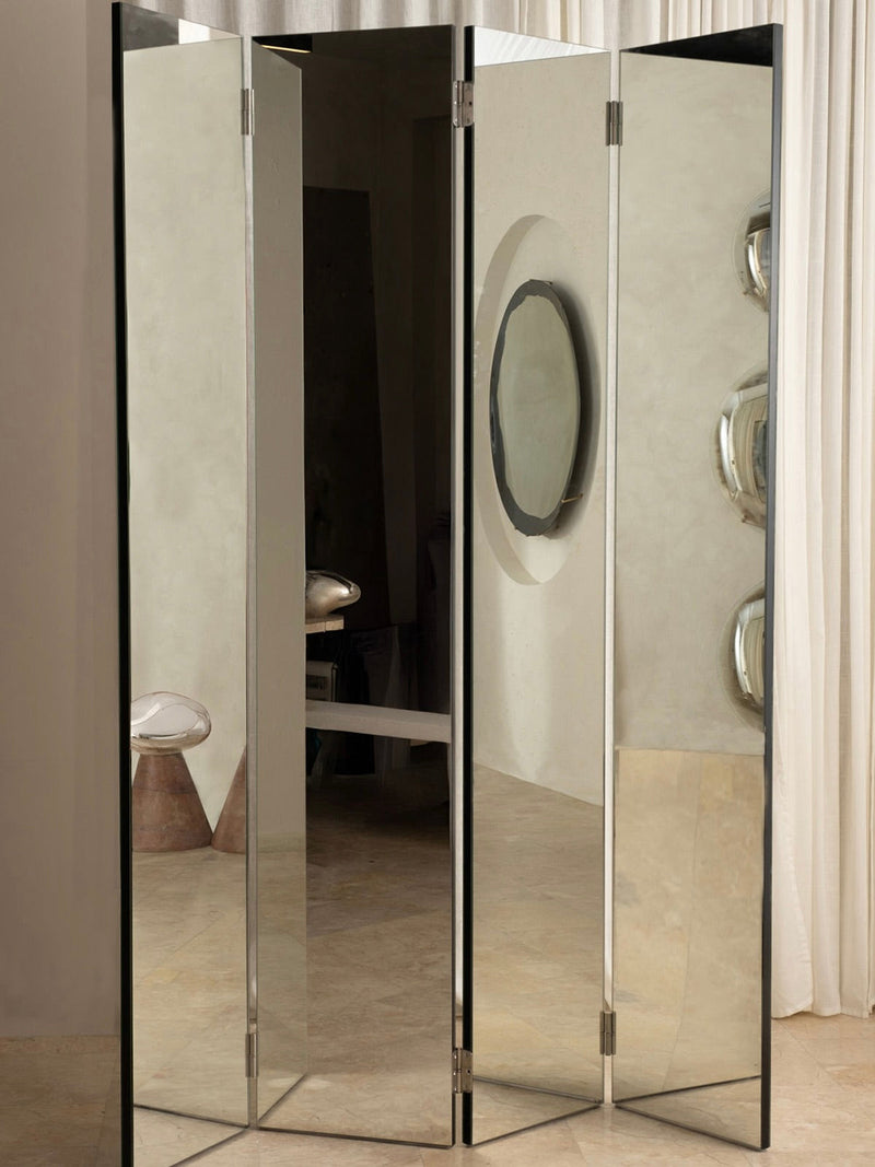 The 'Paravan' Mirror Folding Screen by HOMA stylishly divides a modern room with light curtains, beige walls, circular wall art, and a white dome accent on a brown pedestal.