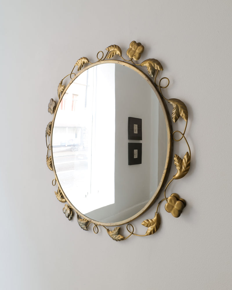The Swedish Modern Brass Mirror 1940s by Collection apart features a gold brass frame with leaf and flower accents, shown mounted on a white wall reflecting a window and two square wall decorations.