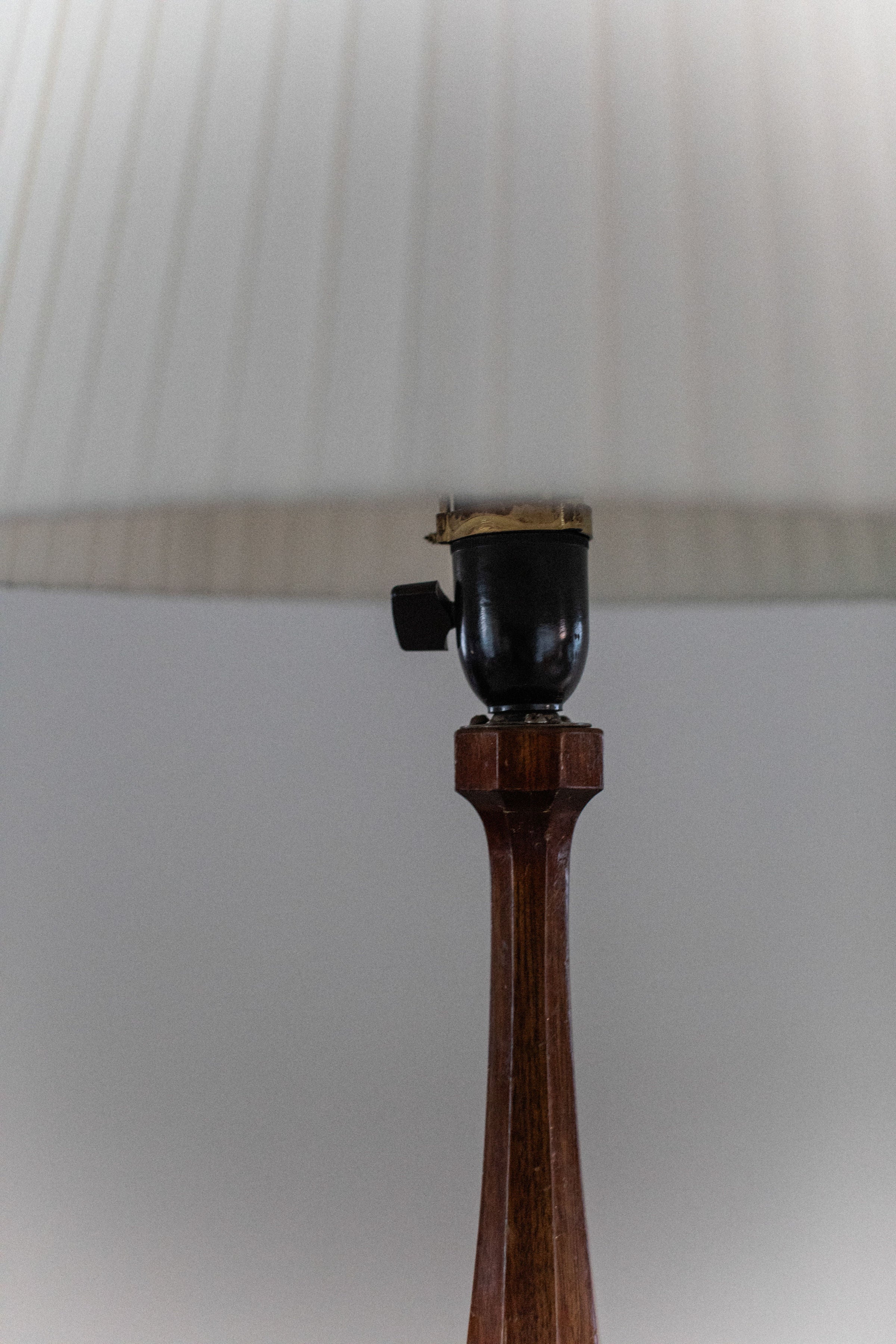A close-up of the 1950’s Table Lamp by Out For Lunch, featuring a wooden base and beige pleated shade, photographed from a low angle with the lampshade partially out of focus.