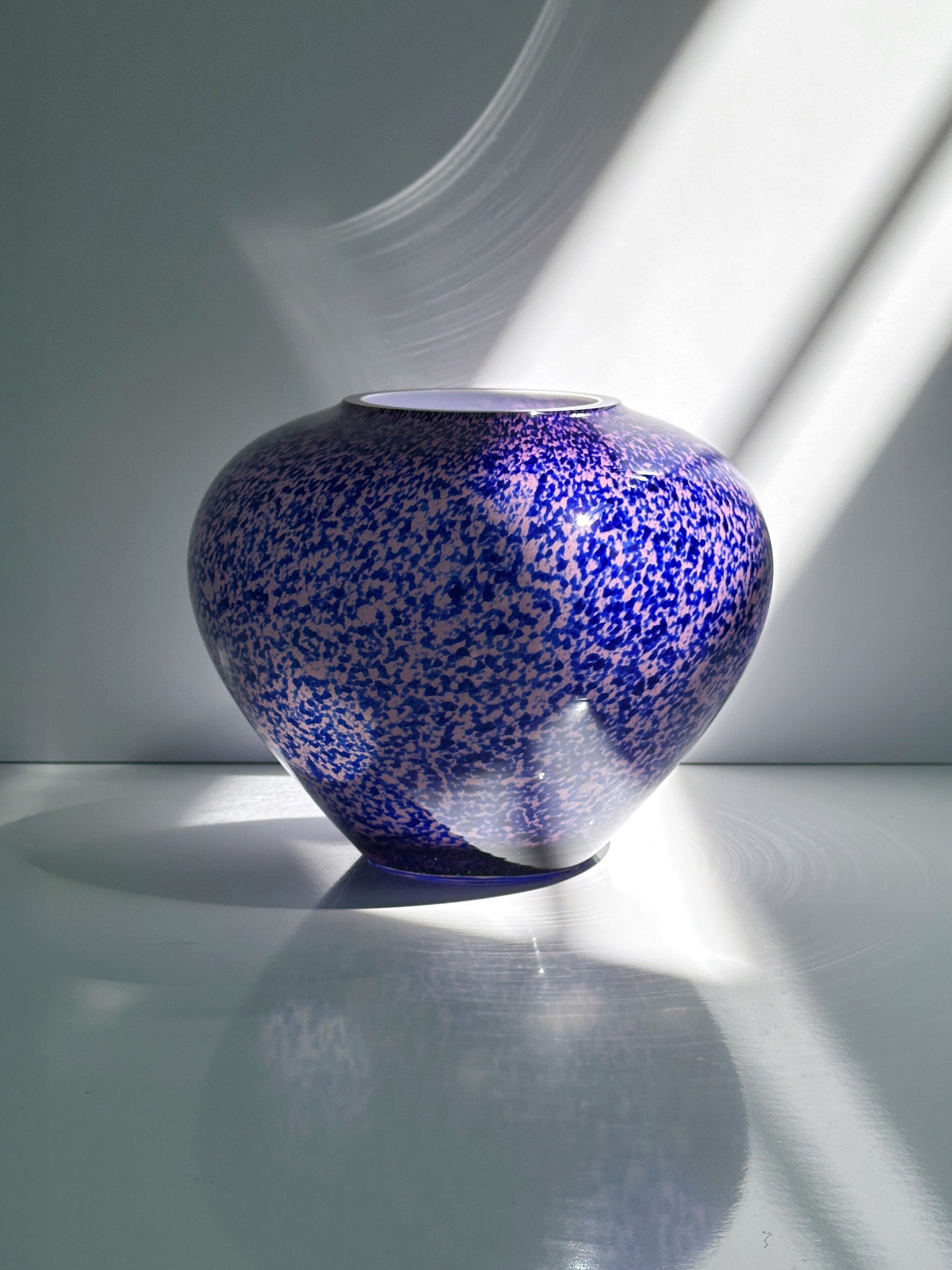 The 1930s Art Deco Tortoise Glass Vase by Dodo Vintage for WMF sits on a white surface, sunlight streaming from the right and casting soft shadows and reflections.