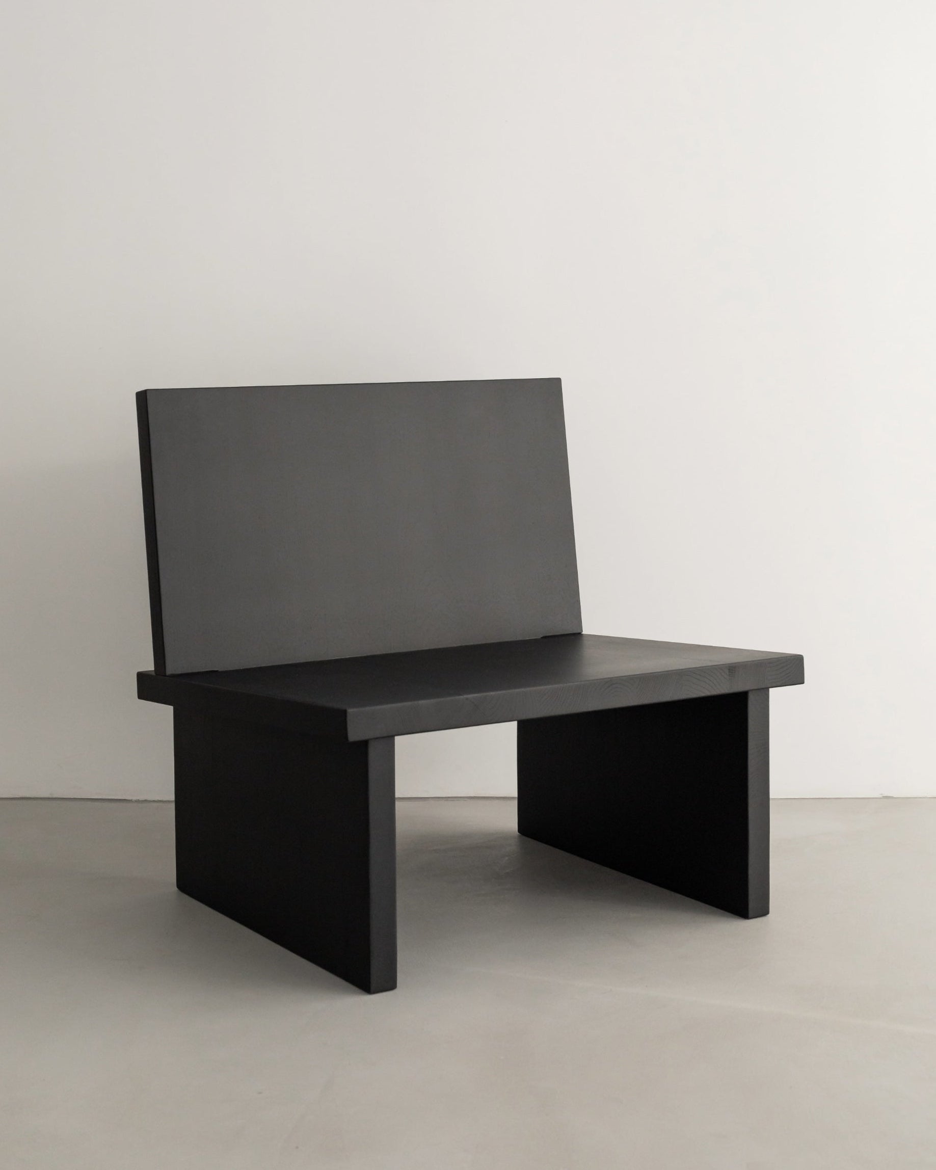 The ZEBU Chair by un'common showcases a minimalist geometric design in solid oak with a natural oil wax finish, featuring a flat seat, straight backrest, and thick side panels, set against a plain white wall on a light floor.