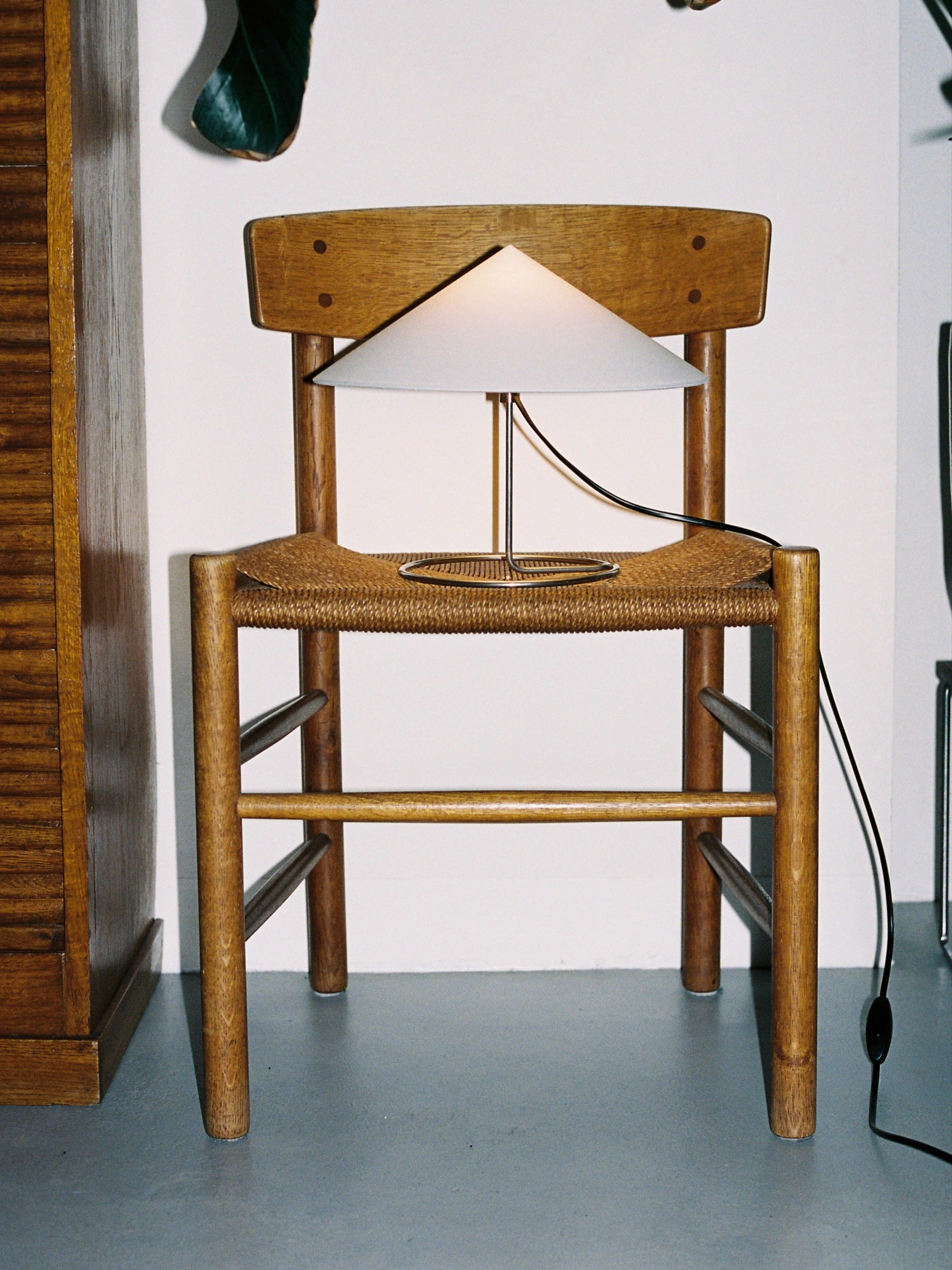 Douli Table Lamp — back view on wooden chair with woven seat