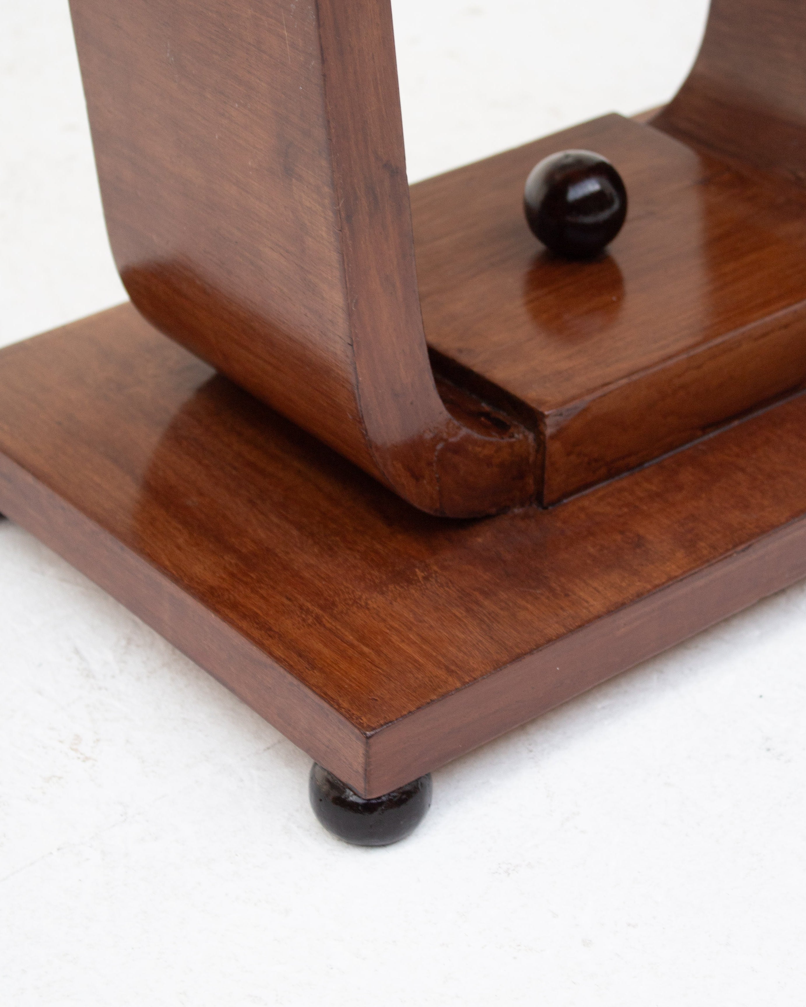 Close-up of the Malata Antwerp Low Art Deco Side Table, featuring a curved leg, narrow profile, square wooden base, dark round feet, and a matching knob—an elegant vintage design set against a white surface.