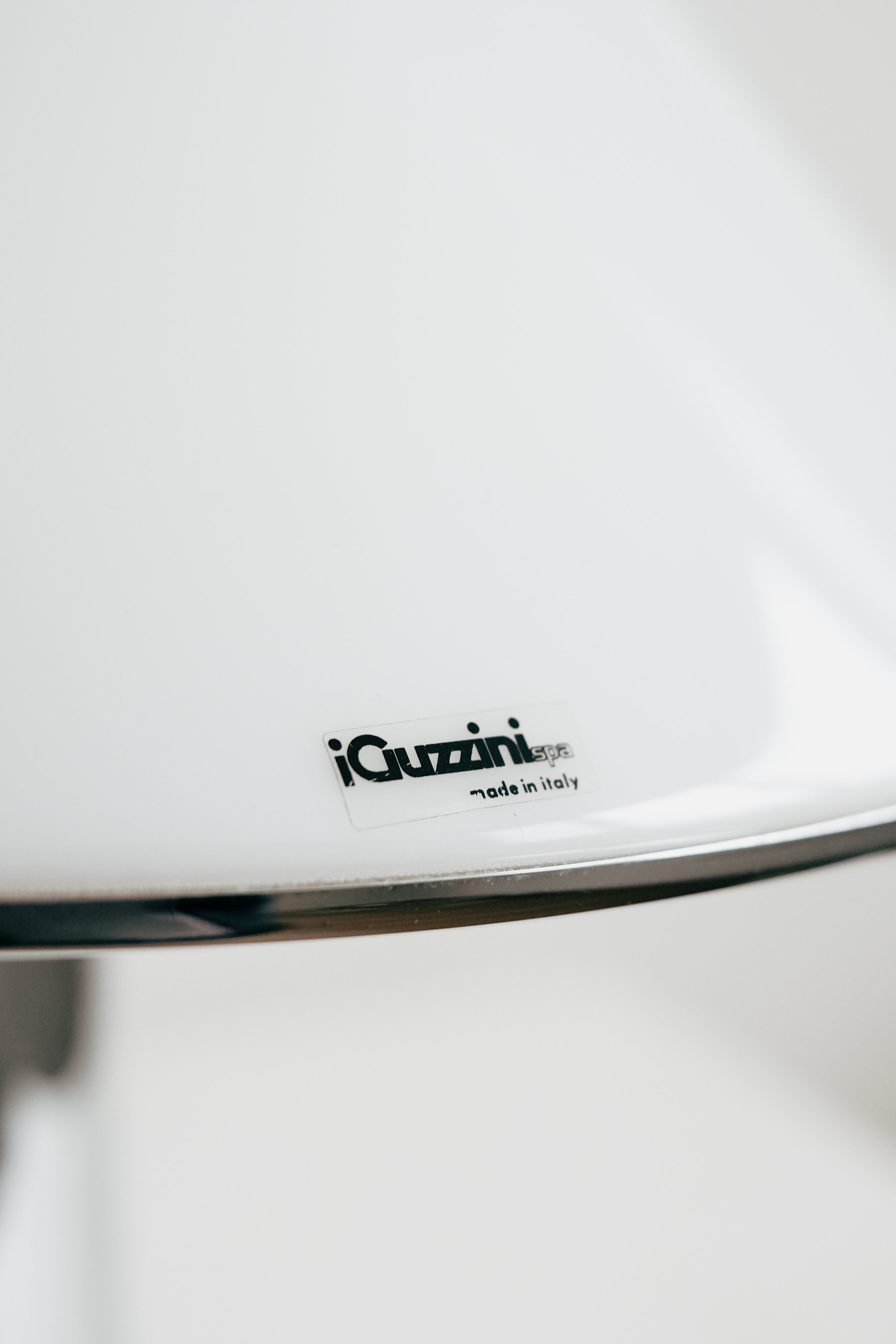 Close-up of a glossy white Harvey Guzzini Elpis Table Lamp by septembre studios, featuring a small "iGuzzini made in Italy" label. The blurred, minimalistic background emphasizes this vintage piece's elegant craftsmanship.