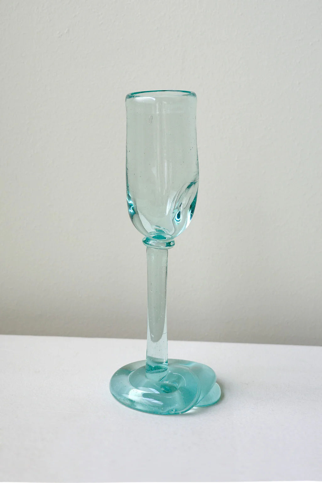 The Thaw - Recycled Flute Glass in Clear by Completedworks features a light blue, sculptural goblet with a wavy base, showcased on a white surface against a pale background—an eye-catching example of contemporary glass art.