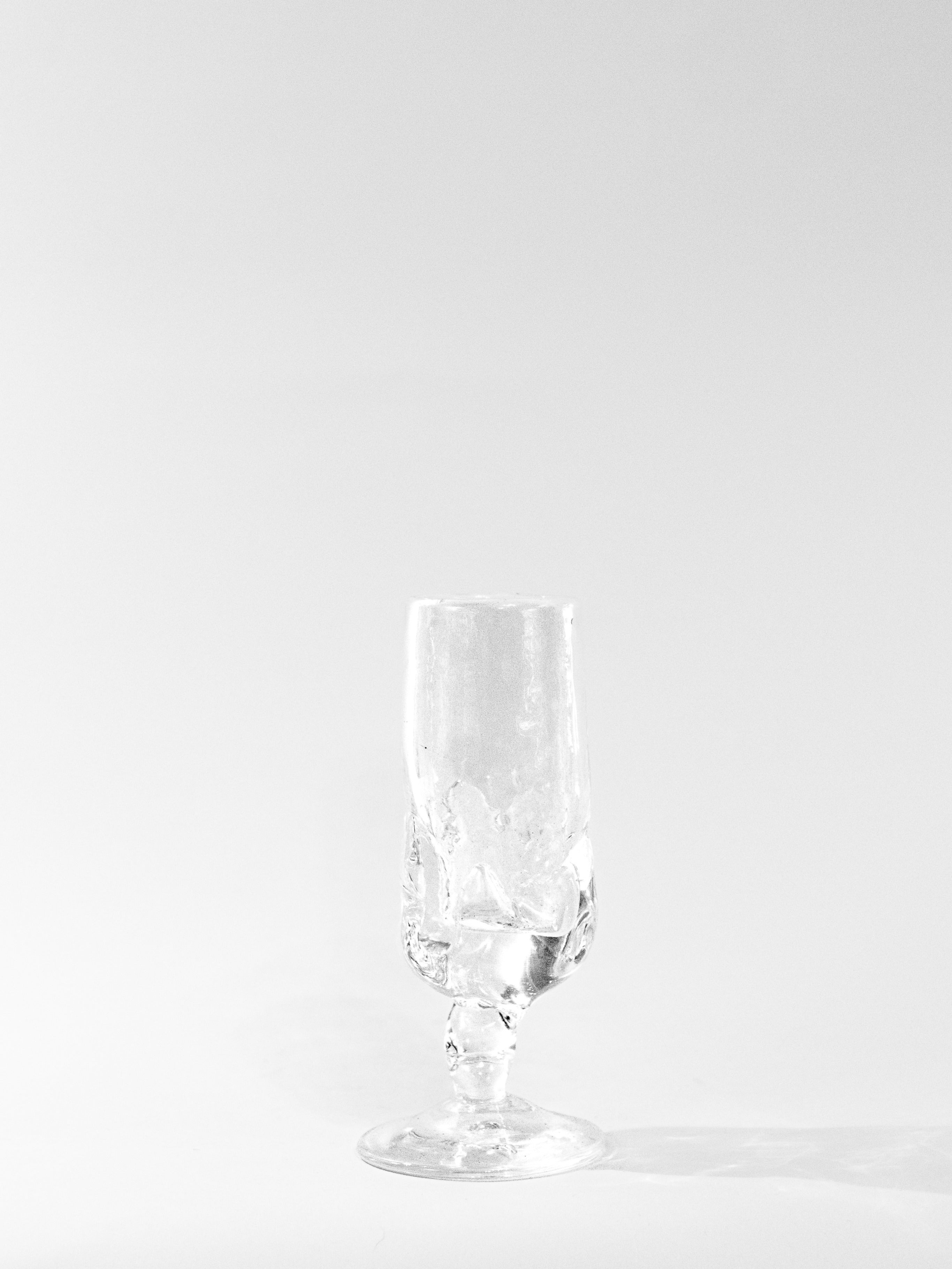 A clear, empty Table Goblet by Szkło Studio with a textured surface stands on a plain white background, casting a soft shadow. The minimalistic, well-lit image highlights the craftsmanship of Szkło Studio.