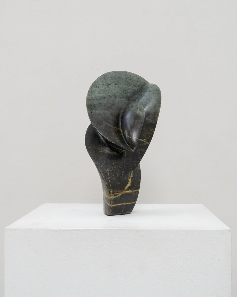 Abstract stone sculpture with curved organic form on white pedestal