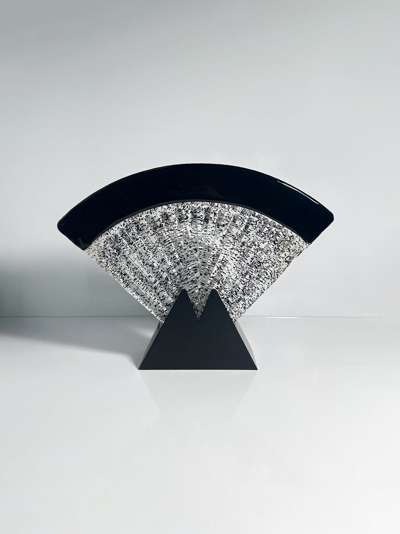 The Large Murano glass fan lamp by Dodo Vintage features a modern abstract Art Deco design, with a black fan-shaped arc and textured silver crescent on a geometric black triangular base, displayed on a reflective white surface.