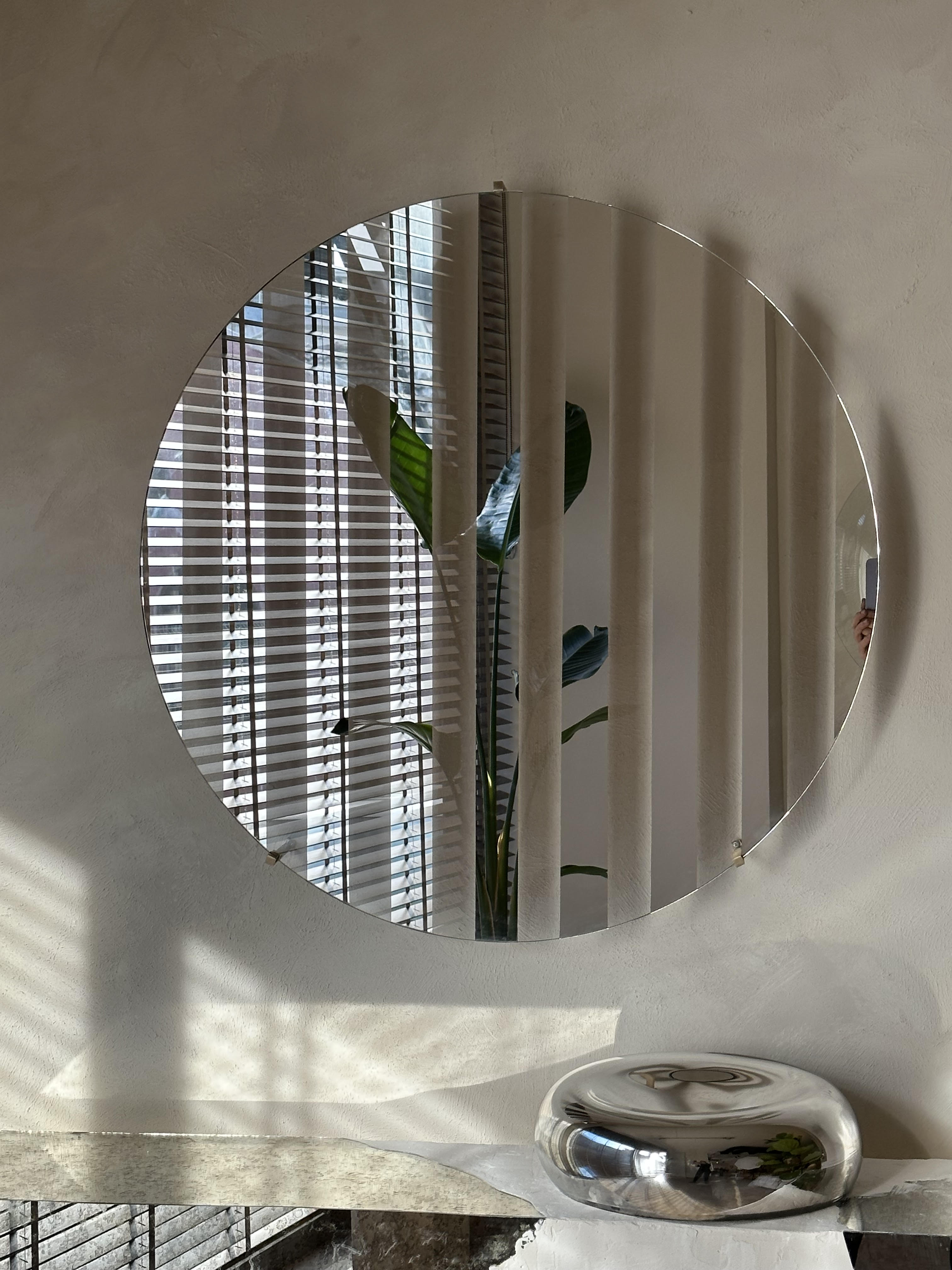 Line III Mirror — round mirror reflecting indoor plant and blinds