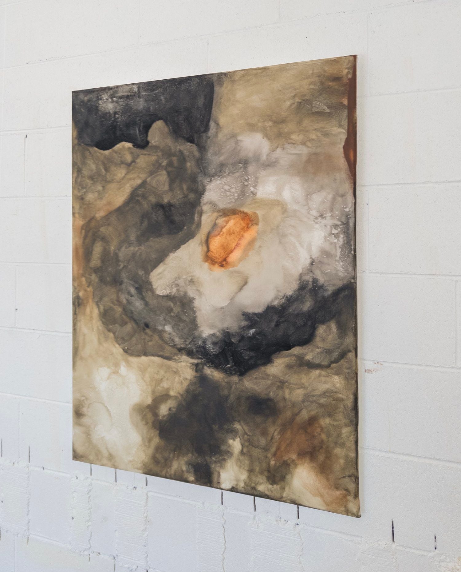 The 'Gracious Tempest' painting by Natasha France is a contemporary abstract artwork featuring swirling brown, black, gray, and white tones with a bold orange center, displayed on a white textured wall.