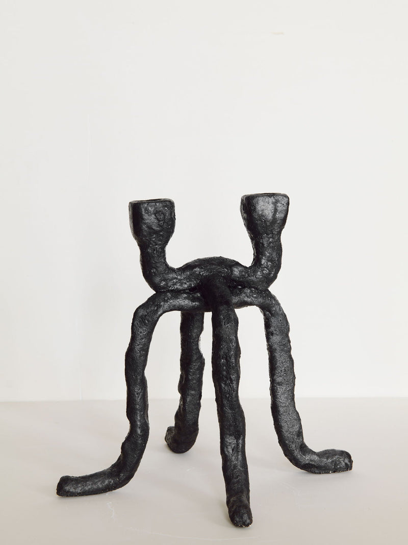 The Candleholder La Chose 2 by Claire Pain is a black, abstract four-legged candle holder with two upward-facing arms. Crafted from white chamotte stoneware, its textured surface adds sculptural appeal—ideal as unique home decor.