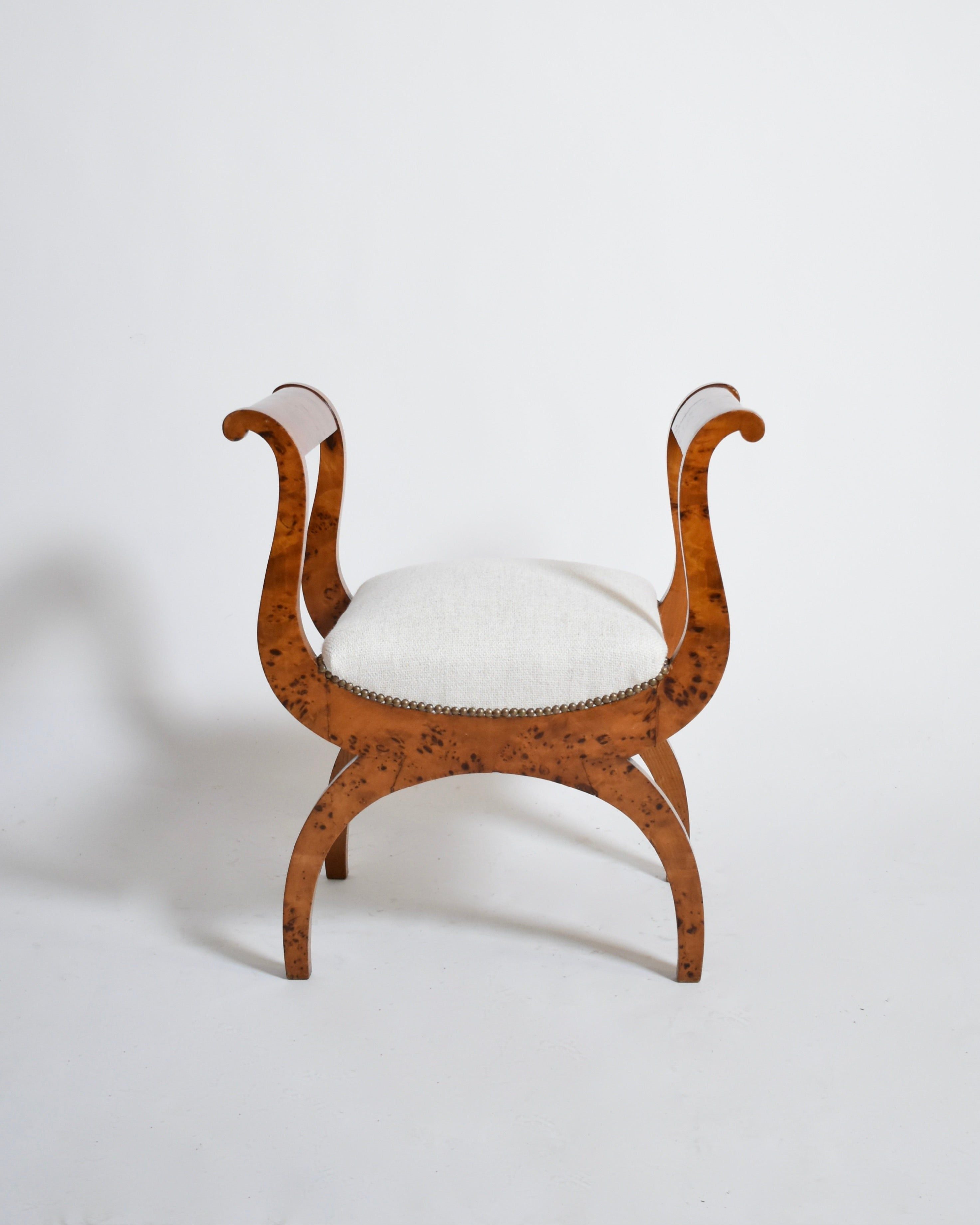 A pair of Walnut Curule Stools, XIXth by Barracuda Interiors features curved swan-neck armrests, a cushioned white seat, and four curved legs, all set against a plain white background.