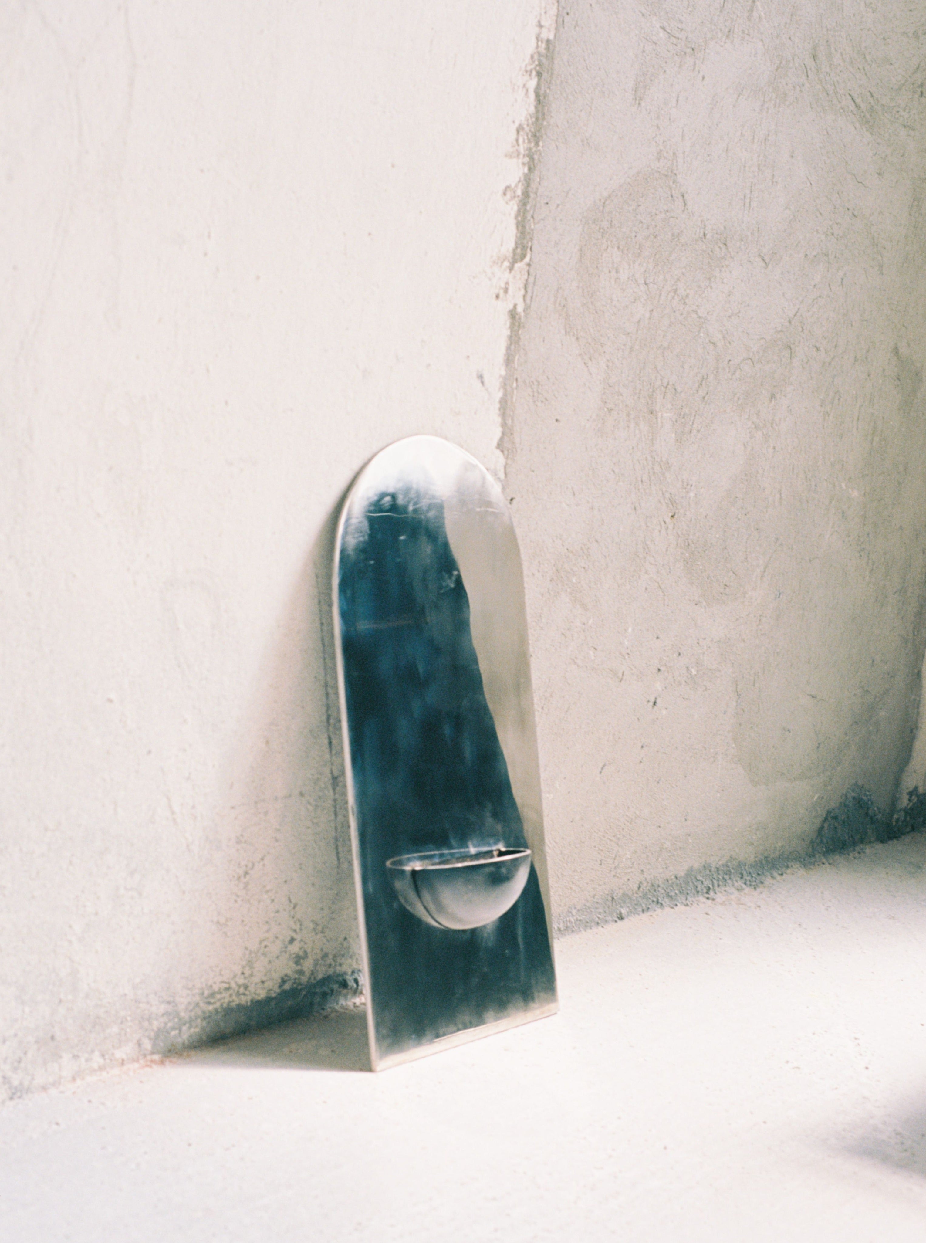 The Mirror of Simple Souls - Contemporary Mirror in Steel — angled view against textured wall