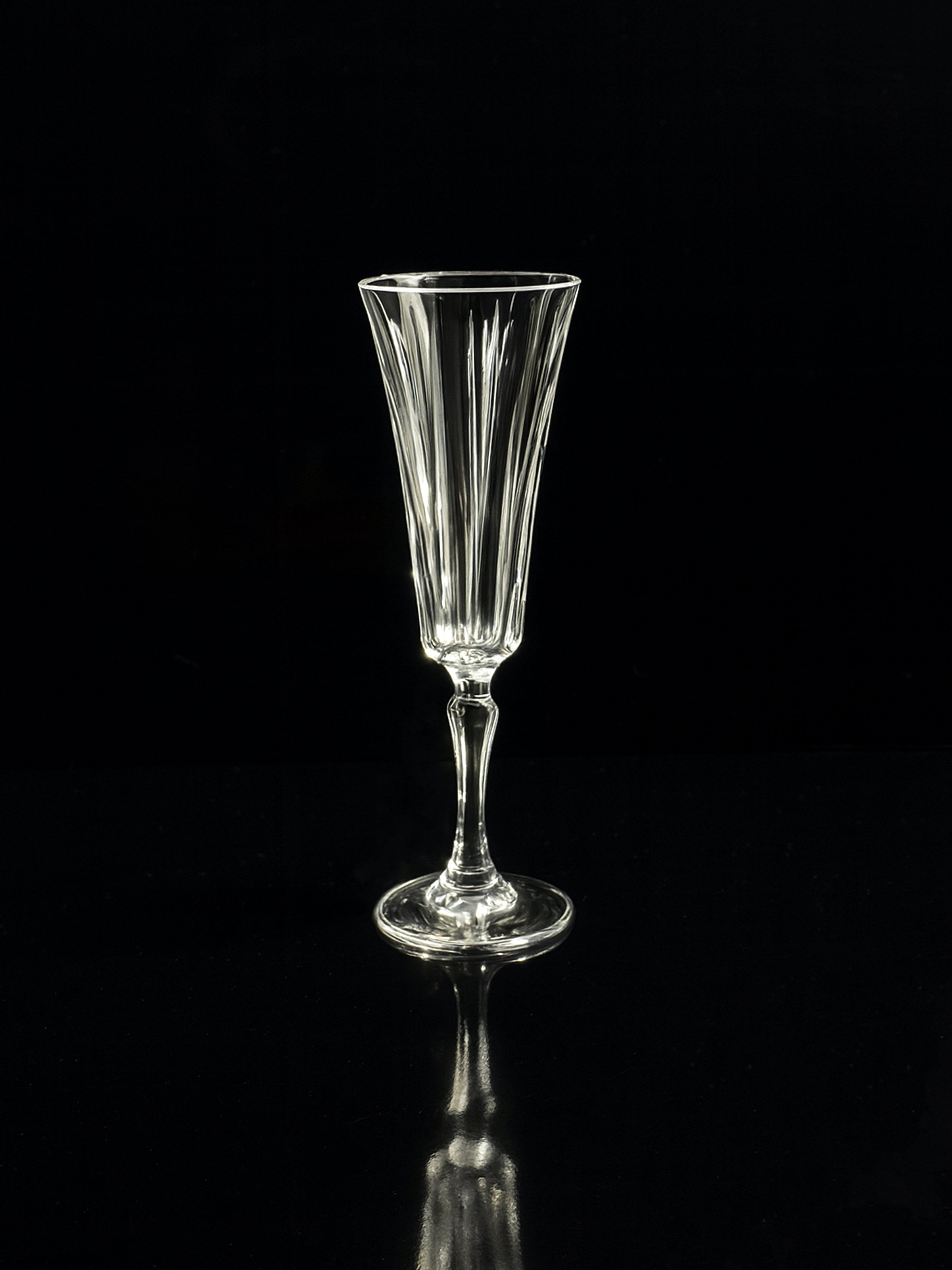 A clear faceted Art Deco crystal flute from Dodo Vintage’s Italian champagne and wine sets stands on a reflective black surface against a black background.