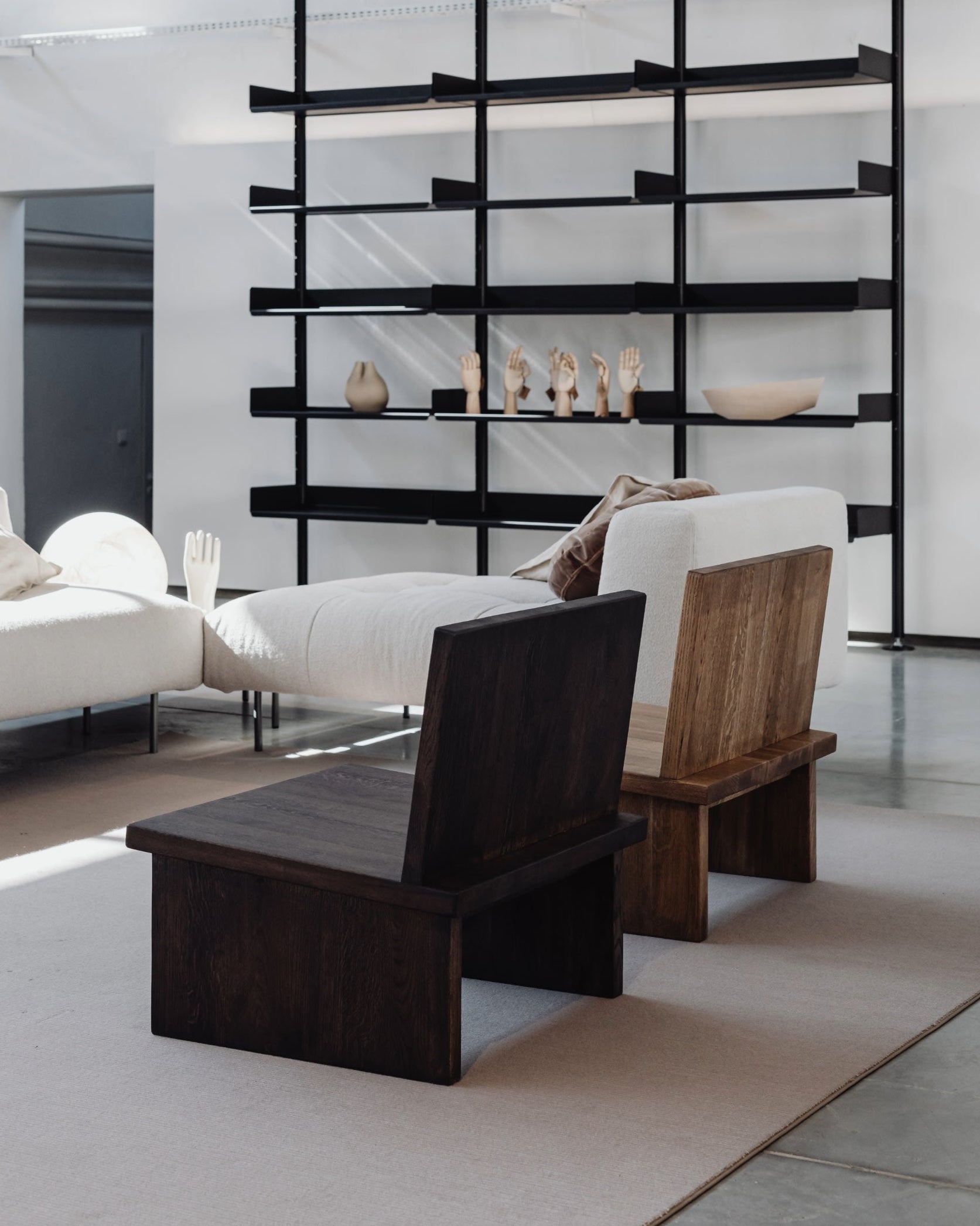 A bright, modern living room features minimalist décor with the un'common ZEBU Chair in solid oak and natural oil wax finish, a white sofa, and a black shelf displaying decorative wooden hands and bowls.