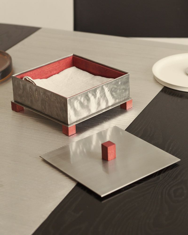 Modern silver napkin box with red interior and wooden feet on dining table
