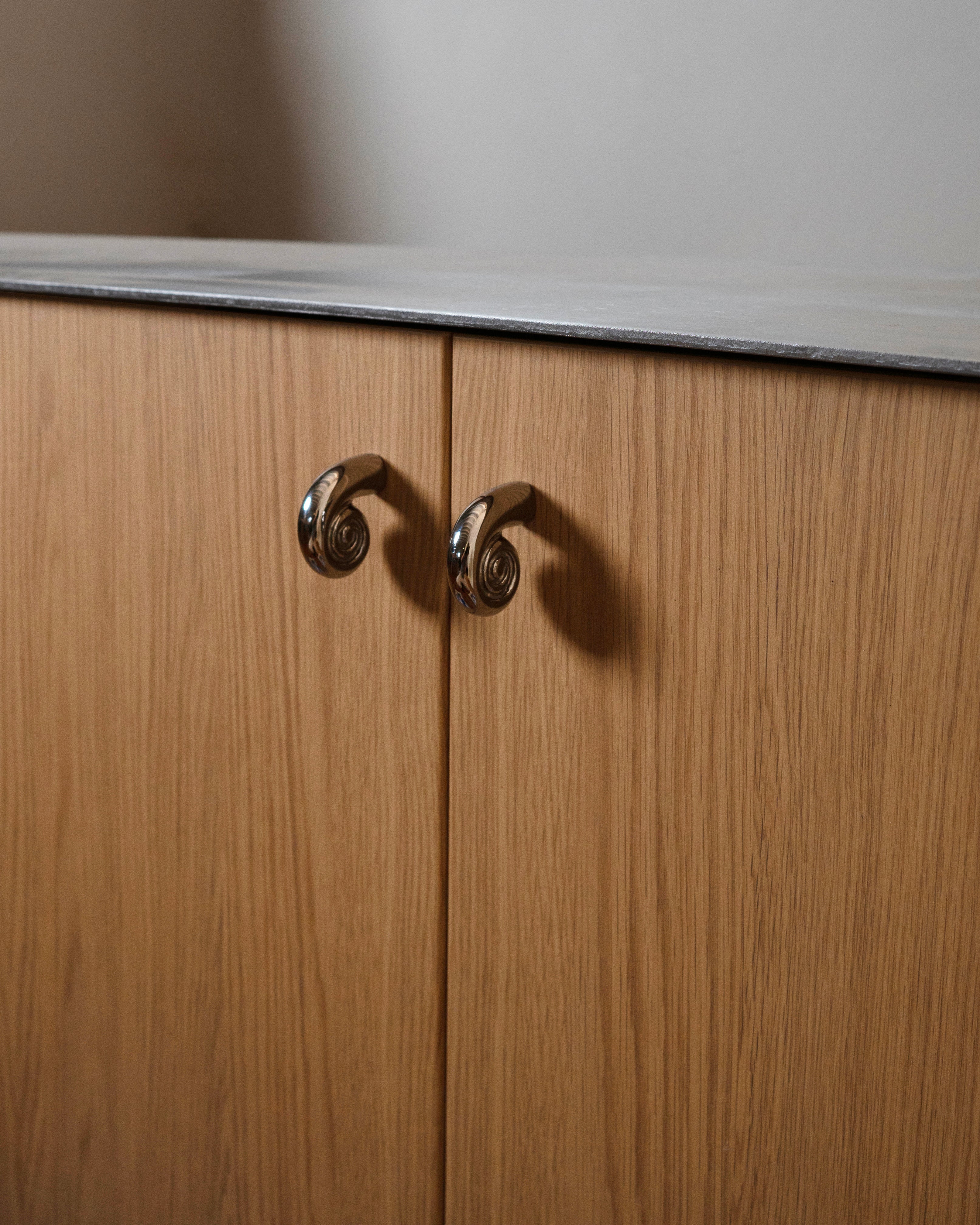 Noelle Knob - Titanium — top view of curved metallic knob on wood cabinet