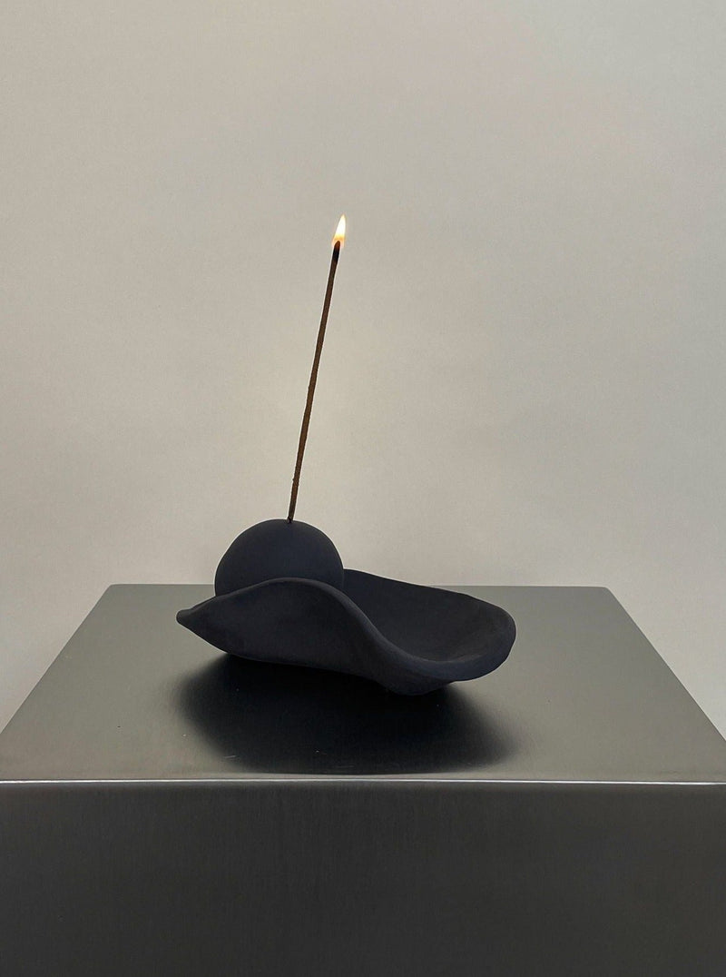 Black stoneware incense holder with lit incense stick on table