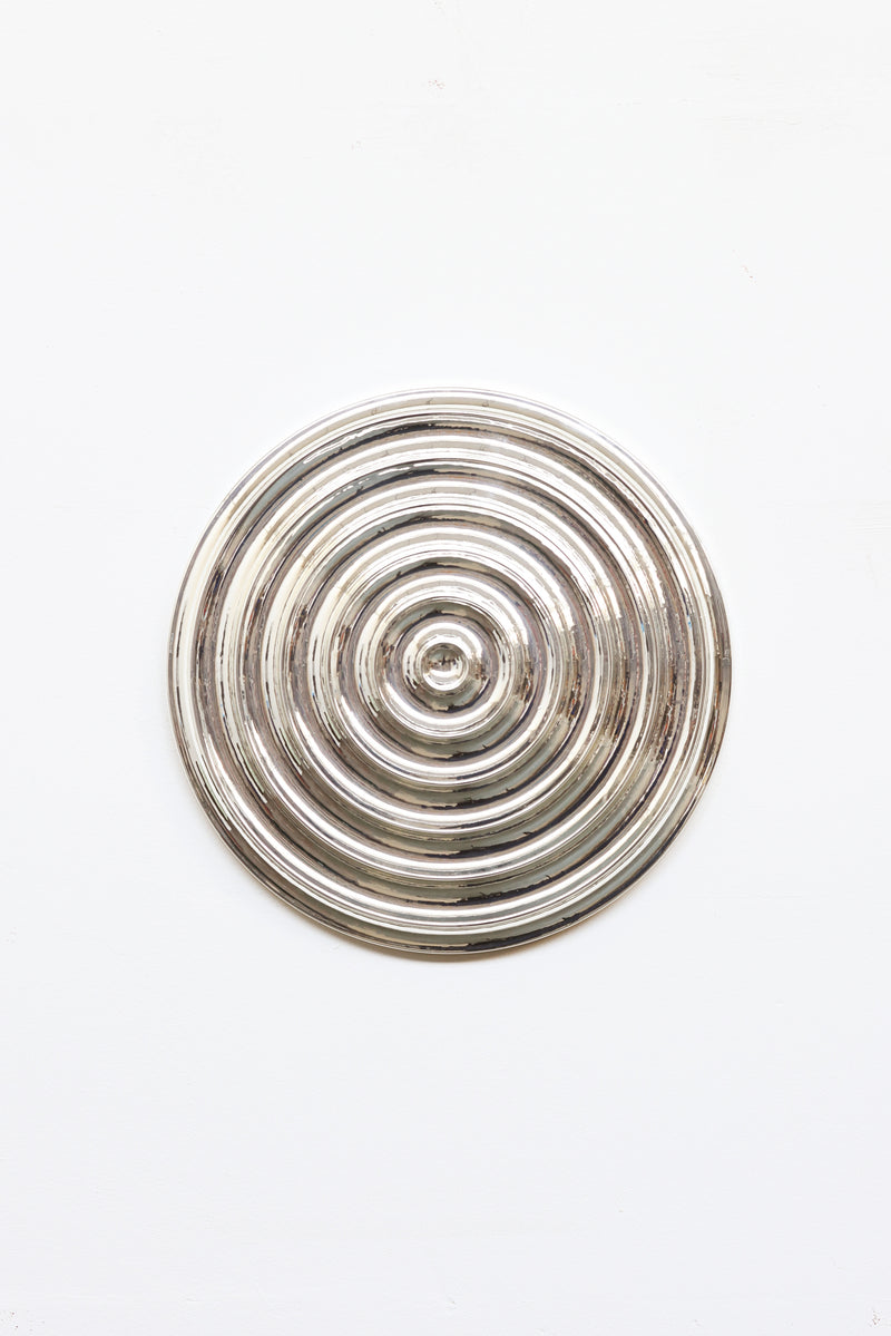 The Klaveroog by Studio Arno Hoogland is a shiny, metallic circular object with concentric raised rings, centered on a plain white background. Its Wave Chrome Silver surface reflects light for a polished, mirror-like look.