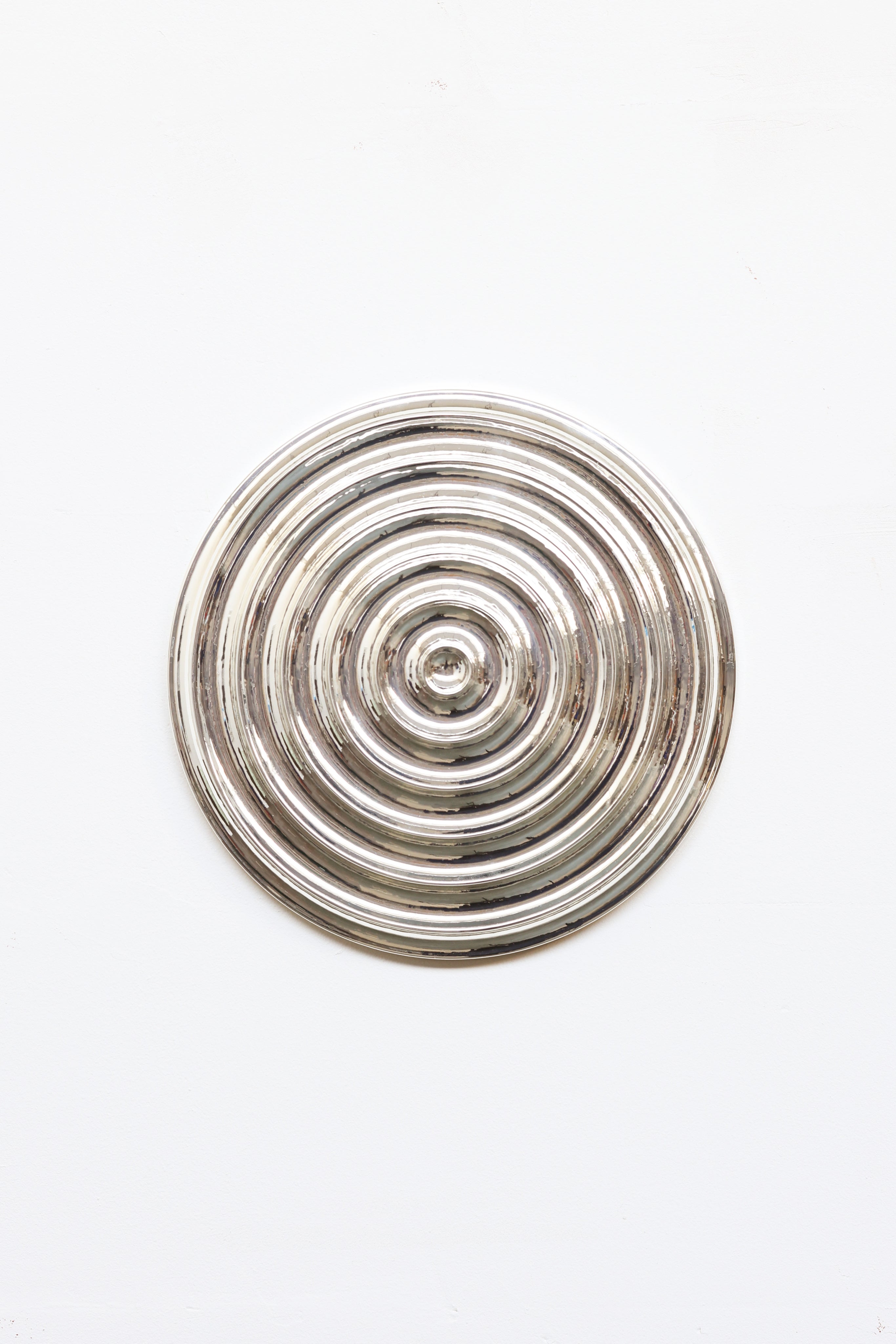 The Klaveroog by Studio Arno Hoogland is a shiny, metallic circular object with concentric raised rings, centered on a plain white background. Its Wave Chrome Silver surface reflects light for a polished, mirror-like look.